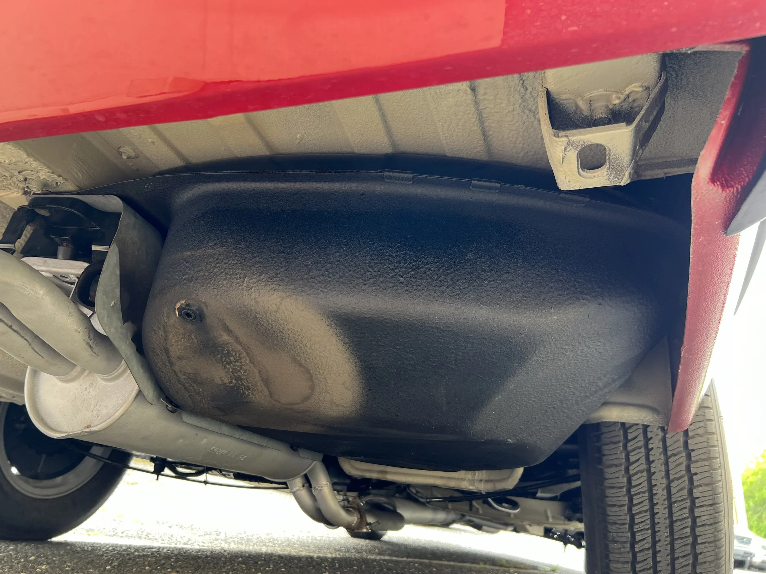 Under the 1977 BMW 630 csi, showing the fuel tank, exhaust pipe, rear wheel and a red frame