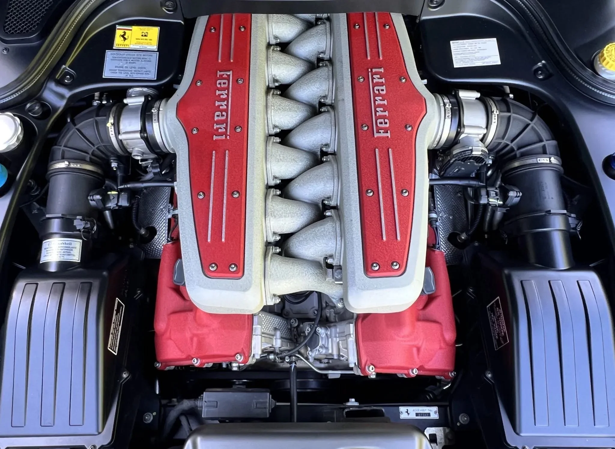 Close-up of a Ferrari engine with red engine covers and silver intake manifolds.