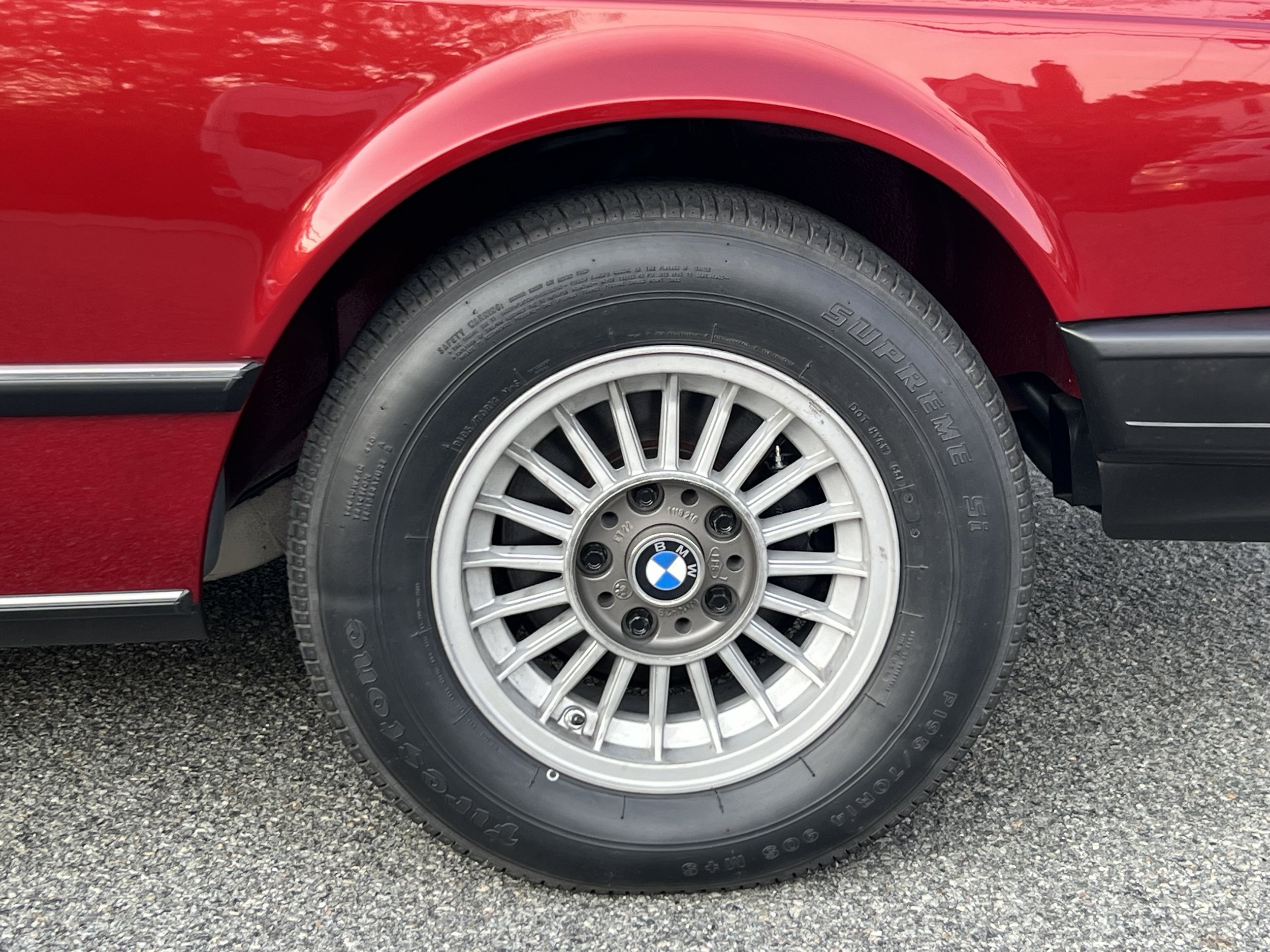 Close-up of a BMW BMW 630 csi wheel with a black tire and silver alloy rim, part of a red car parked on asphalt.