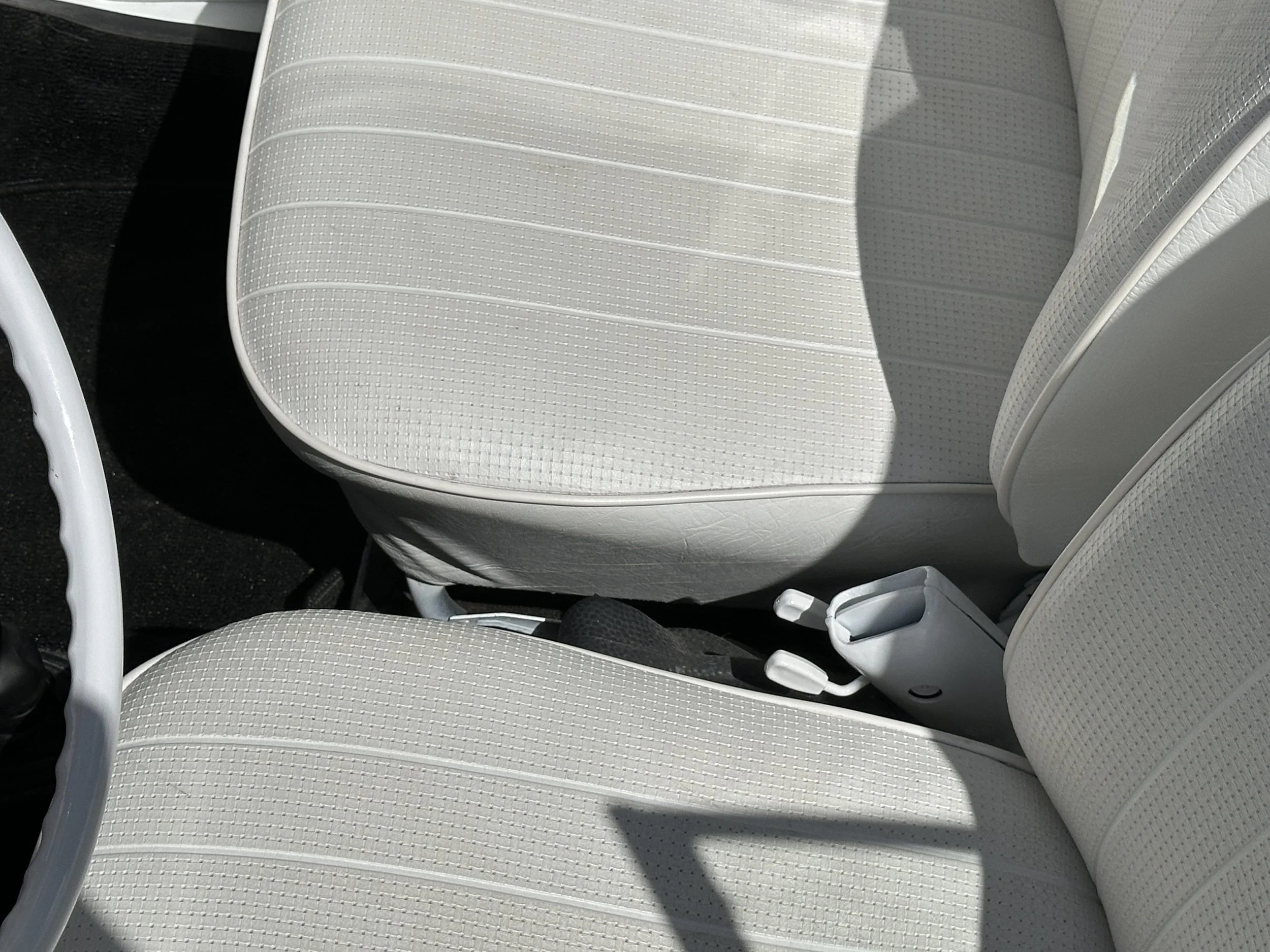 Close-up of the front passenger and driver seats in a vintage car, upholstered in white vinyl with a textured pattern, and a white center console between them.