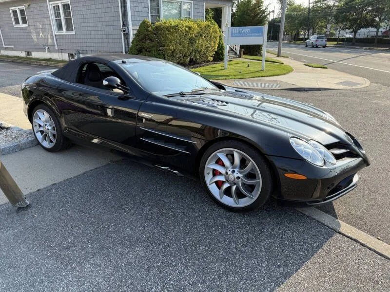 A black convertible sports car parked on a city street sidewalk.