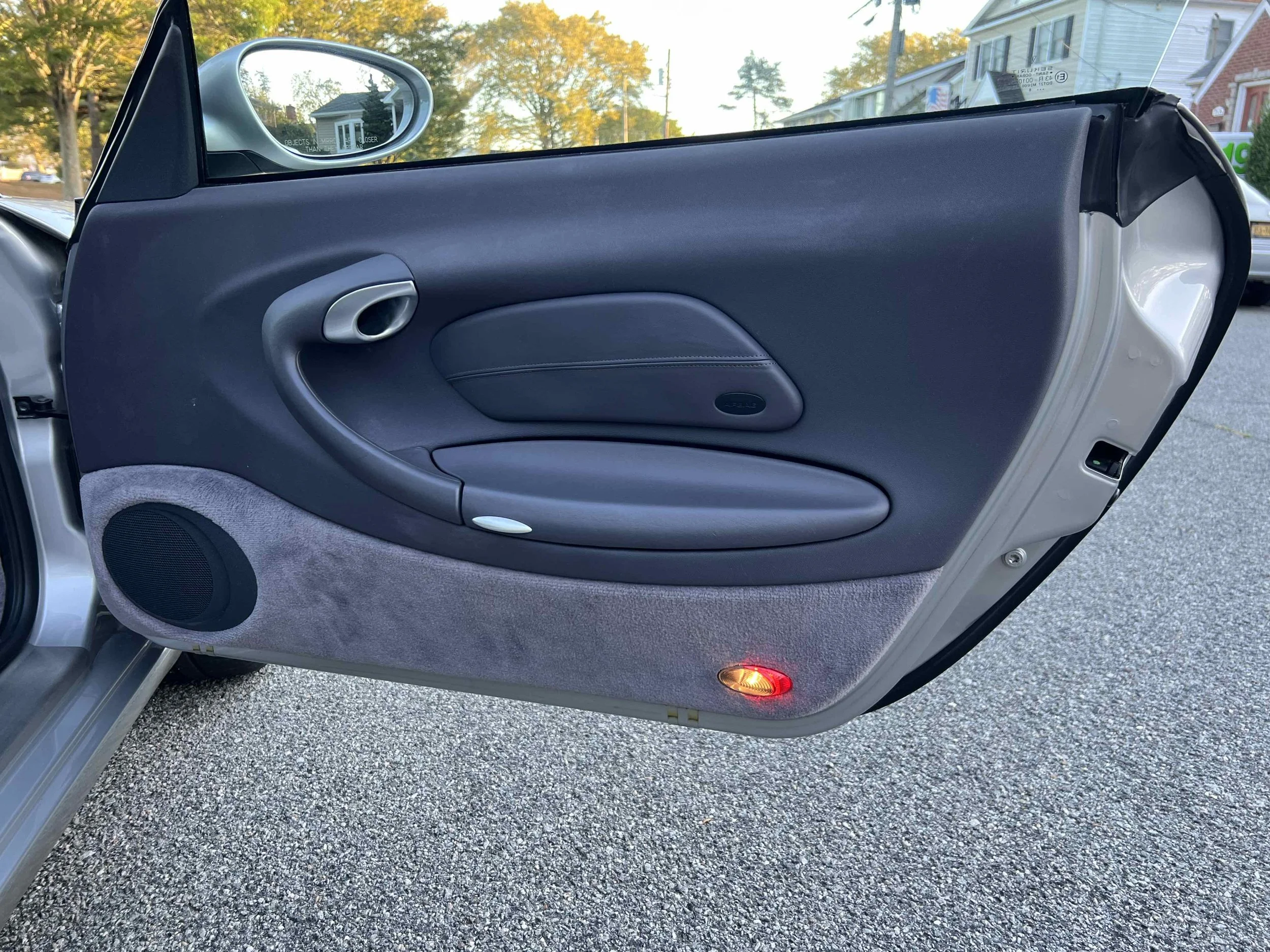 Close-up of a car door interior featuring a speaker, door handle, and a red light in a residential neighborhood.