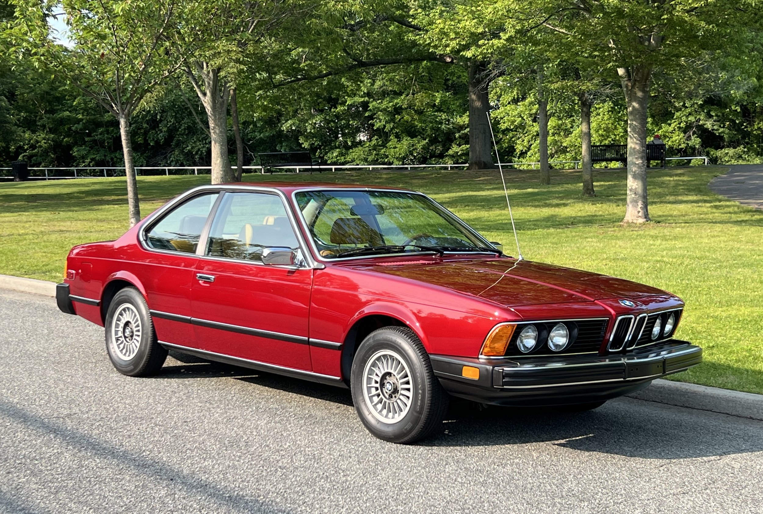 Ruby Red 1977 BMW 630 csi on display in park with trees and grass in background for sale at FlowHaus
