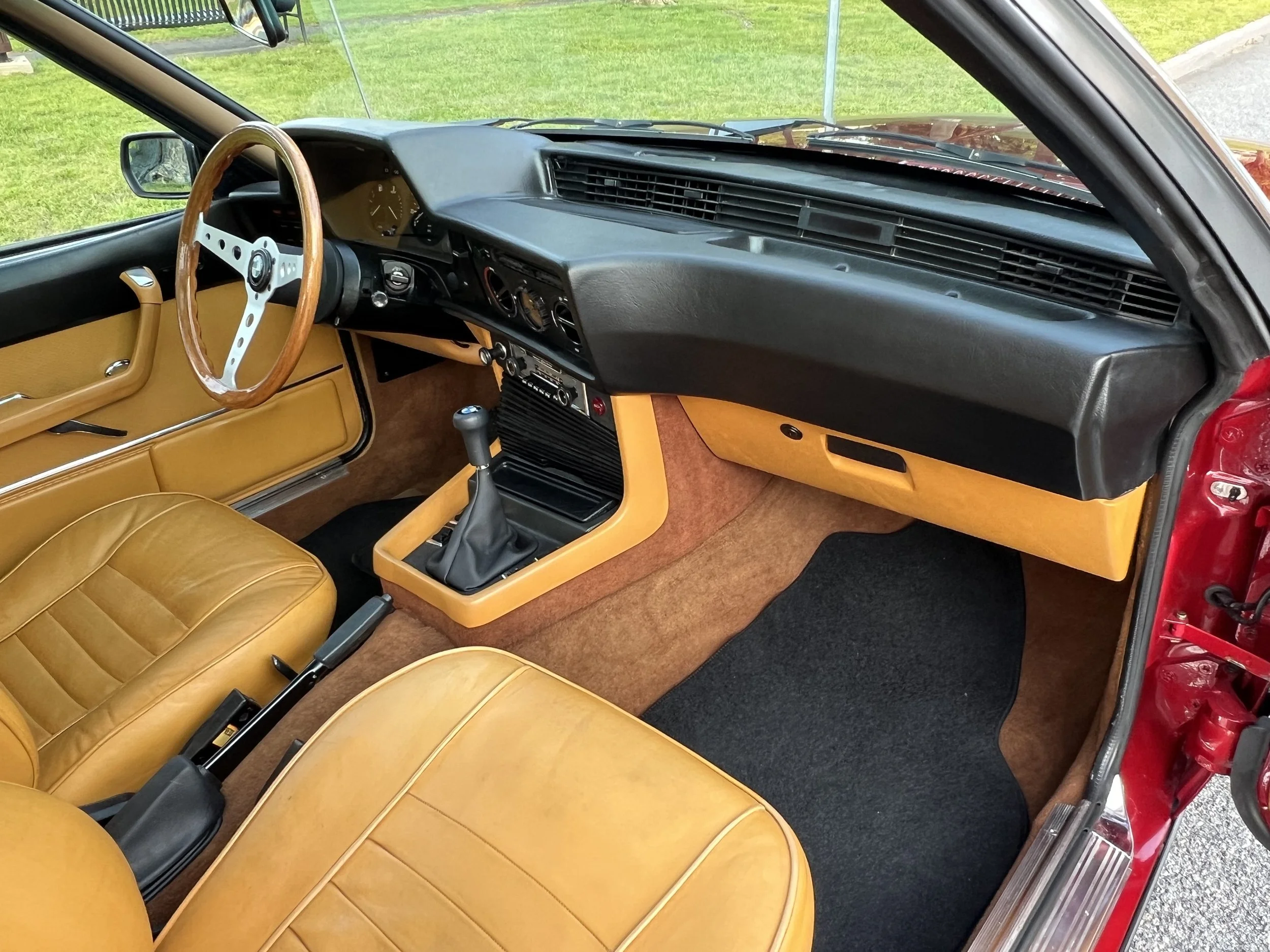 Interior of a vintage BMW 630 csi car with tan leather seats, wooden steering wheel, black dashboard, and manual transmission gear shift.
