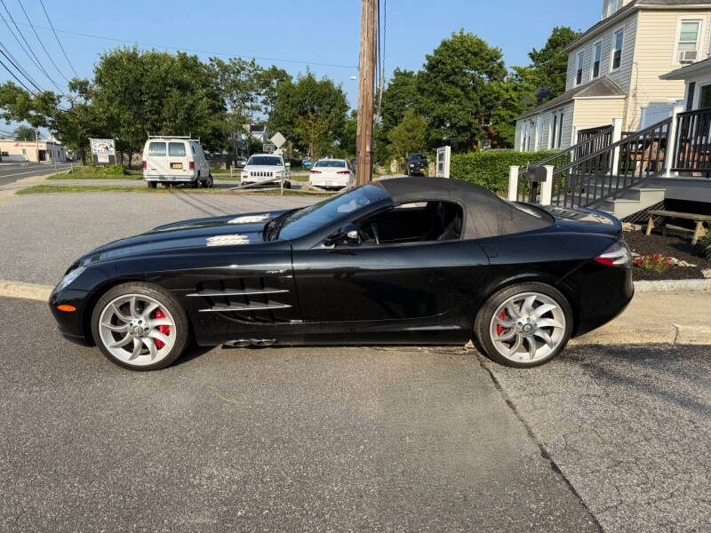 A black convertible sports car parked on the street with houses and trees in the background.