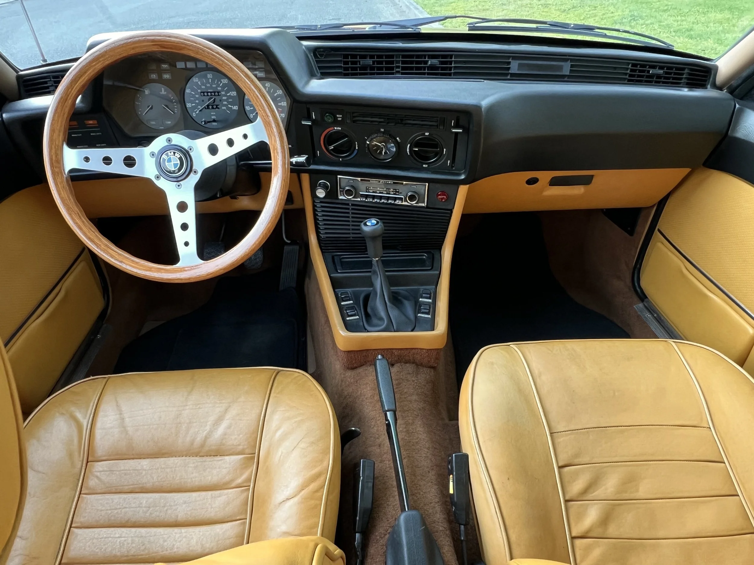 Interior of a classic BMW BMW 630 csi car with yellow leather seats, wooden steering wheel, and black dashboard featuring a speedometer, tachometer, and vintage radio.