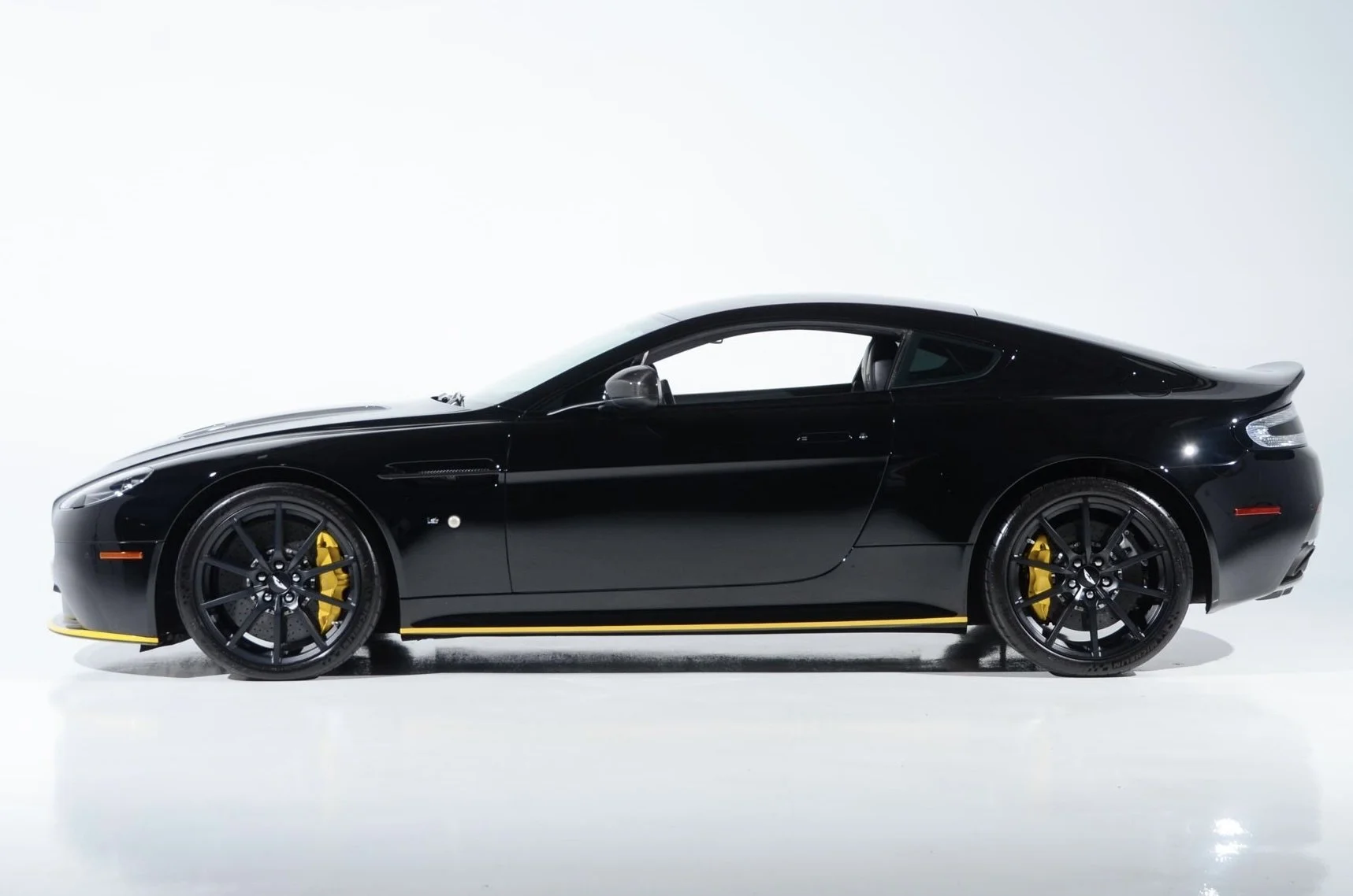 Side view of a sleek black sports car with yellow brake calipers, set against a plain light background.