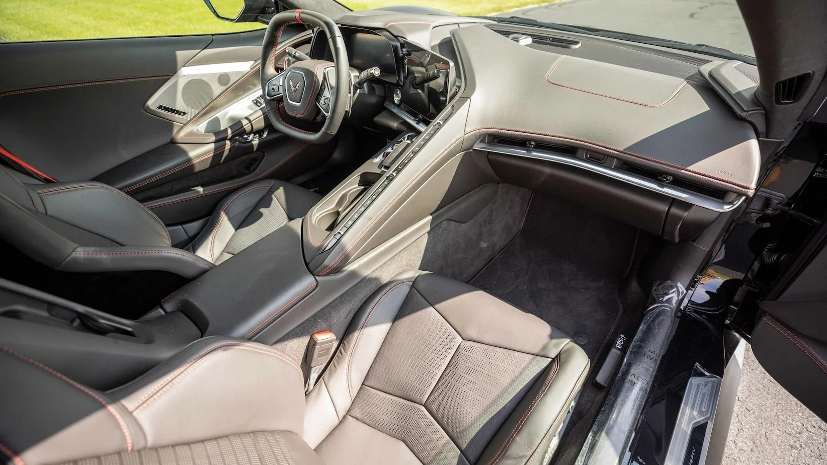 Interior view of a modern sports car with a black and beige leather interior, focusing on the dashboard, steering wheel with Corvette logo, and front seats with red stitching.