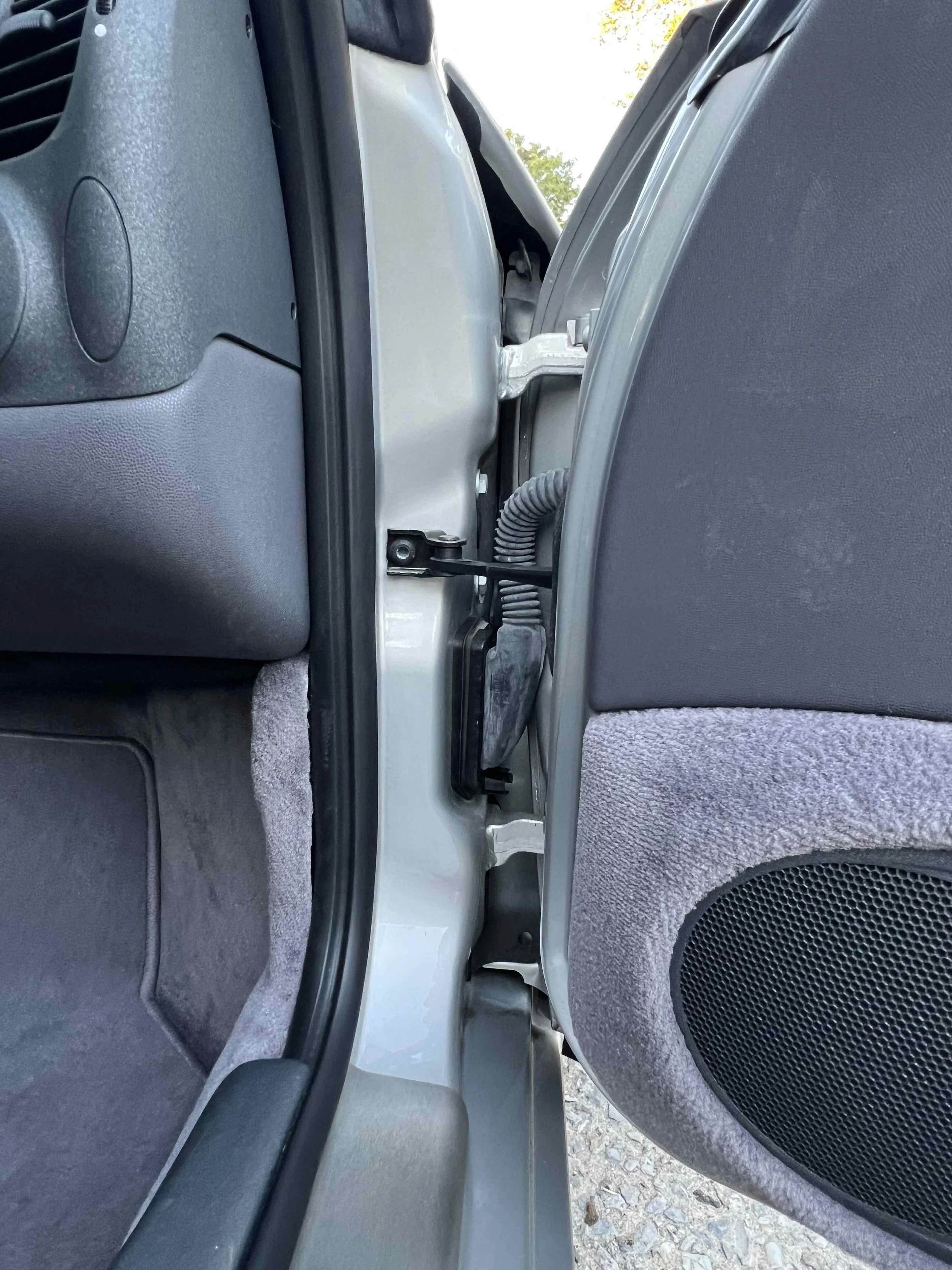 View of the gap between the car door and the vehicle's interior, showing the door hinges and wiring.