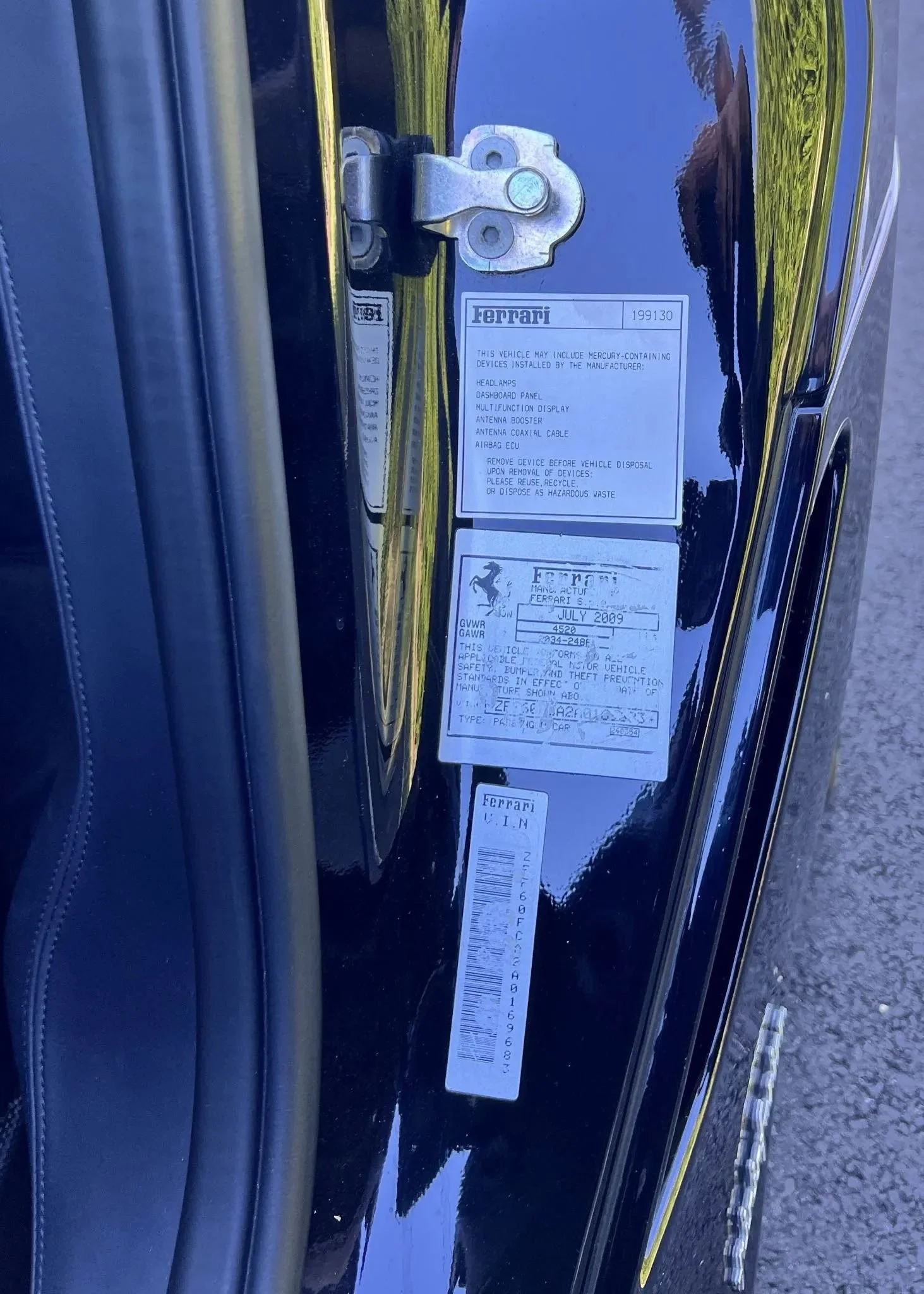 Close-up of the door frame of a black Ferrari 458, showing the manufacturer's information labels and the door latch mechanism.