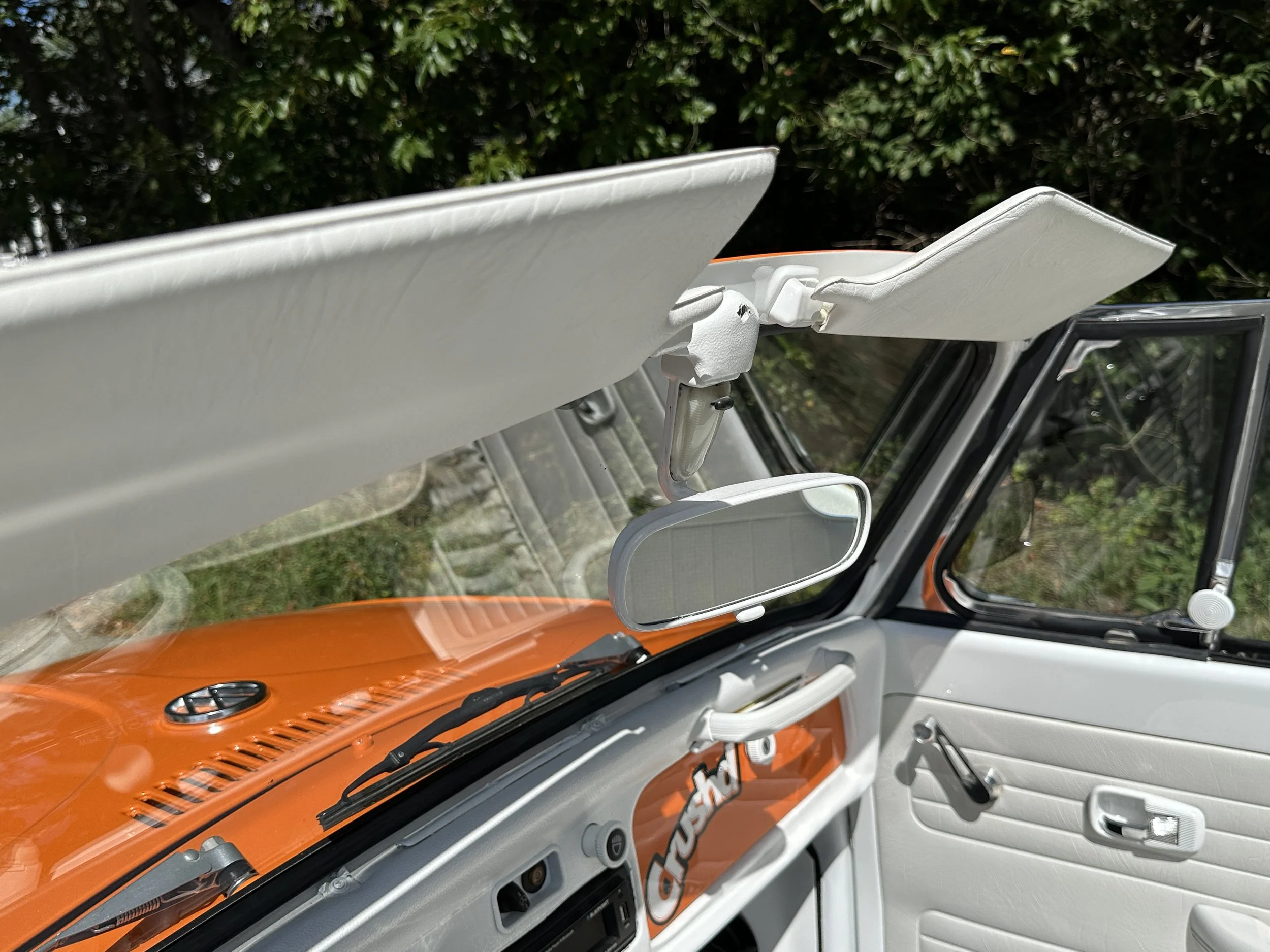 Close-up of the interior of a vintage vehicle, showing the windshield, rearview mirror, sun visors, and dashboard with a partially visible sticker that says 'PEUGEOT' in orange and white.