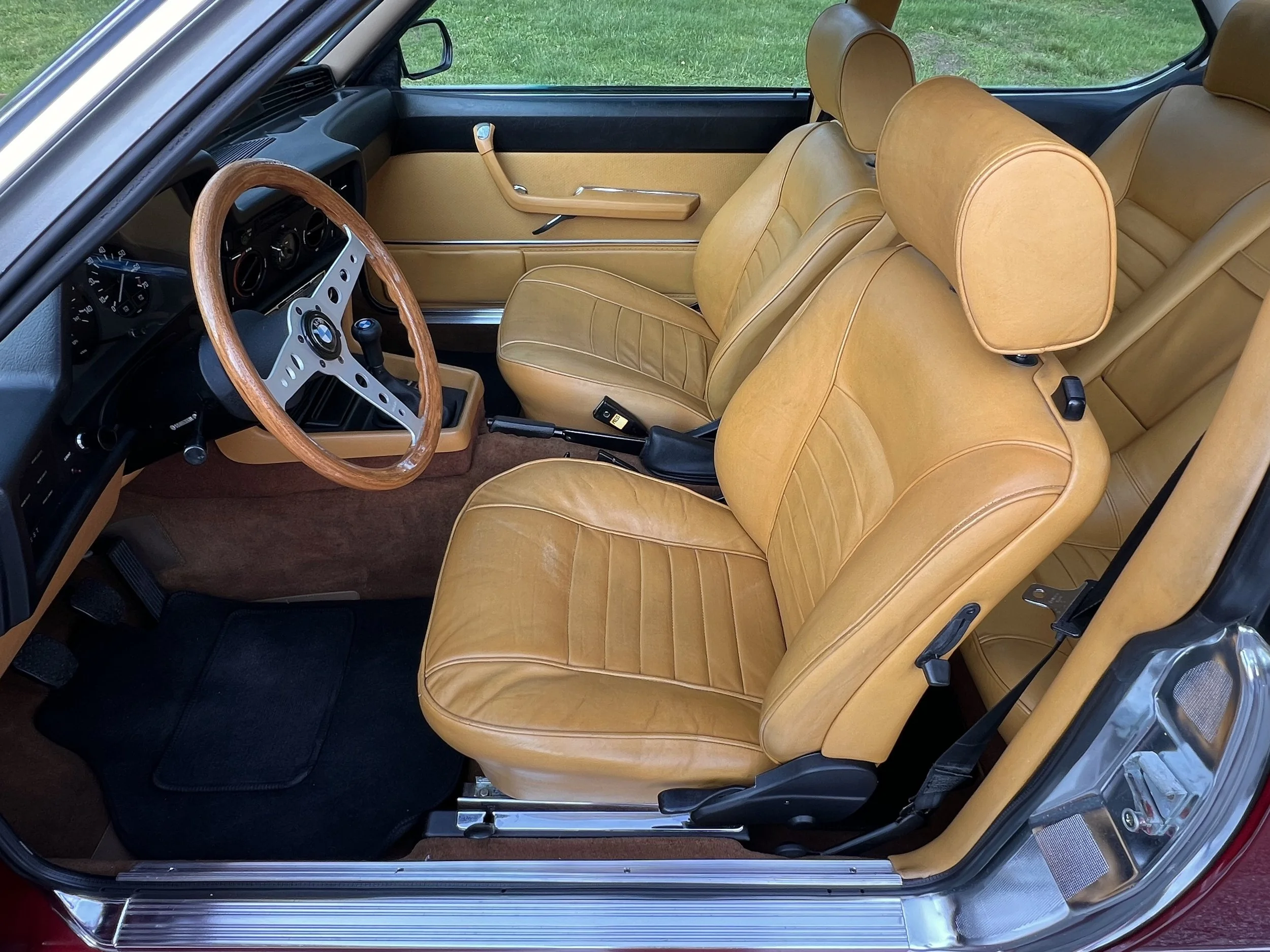 Interior of a vintage BMW BMW 630 csi car with tan leather seats, a wooden steering wheel, and a black dashboard.