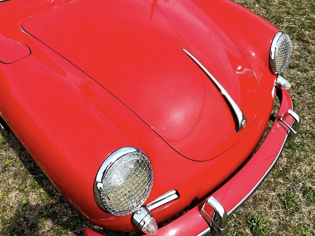 Close-up of a vintage red sports car with round headlights, chrome bumper, and hood ornament, parked on grass.