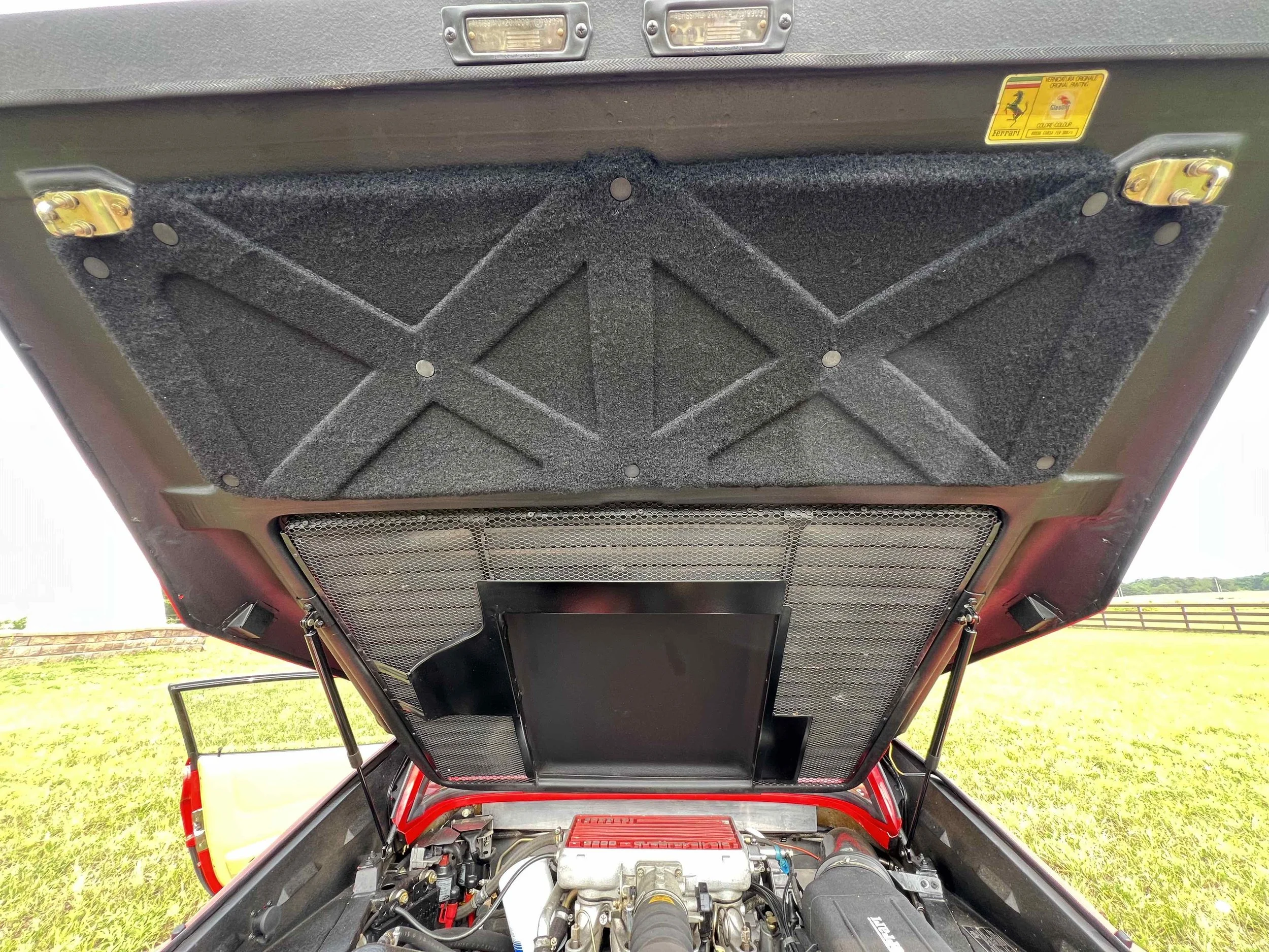 Under the hood of a car with soundproofing material on the underside of the hood and a flat screen mounted in the engine bay.