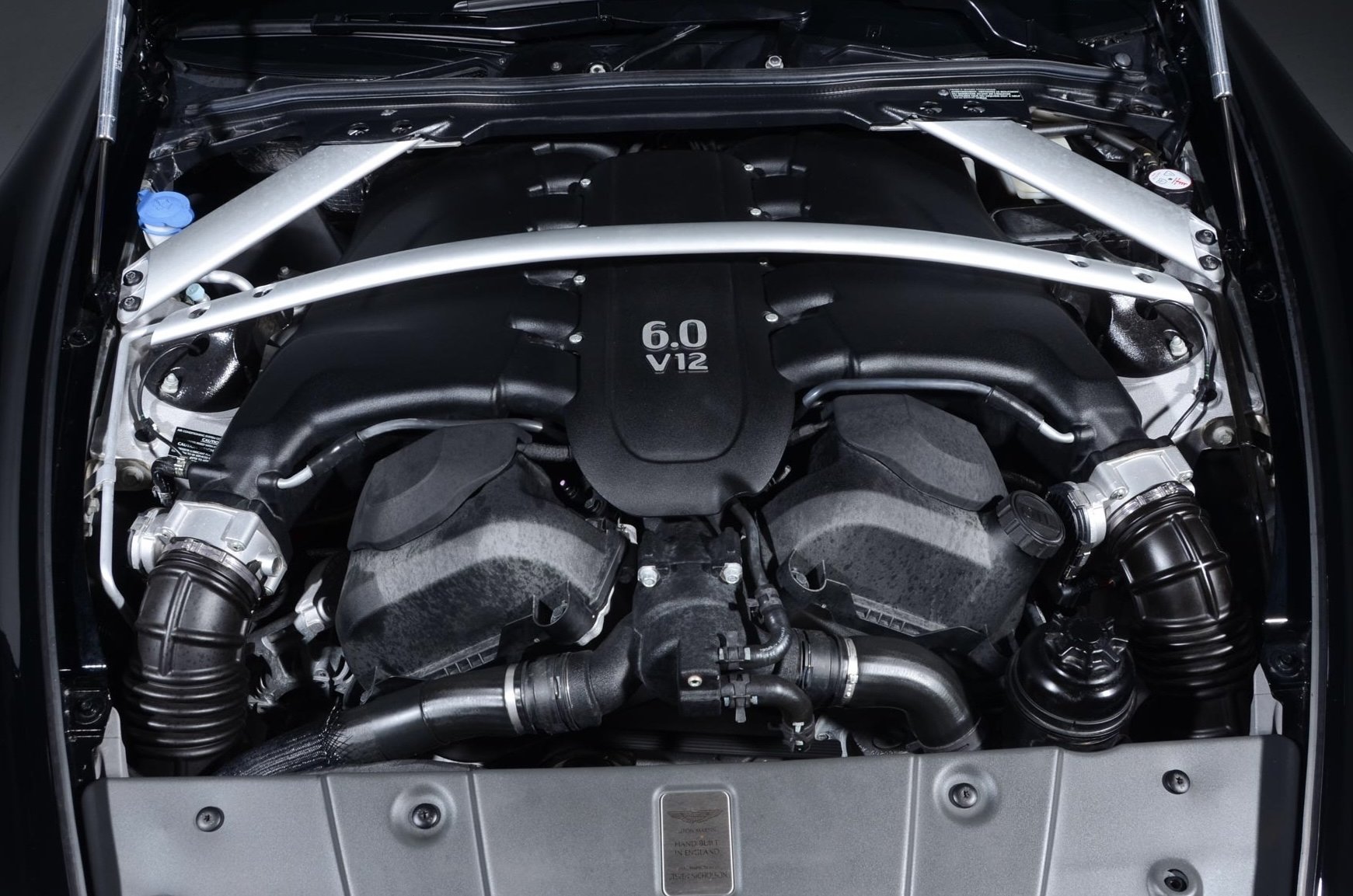 Engine bay of a car with a 6.0-liter V12 engine, showing various hoses and components.