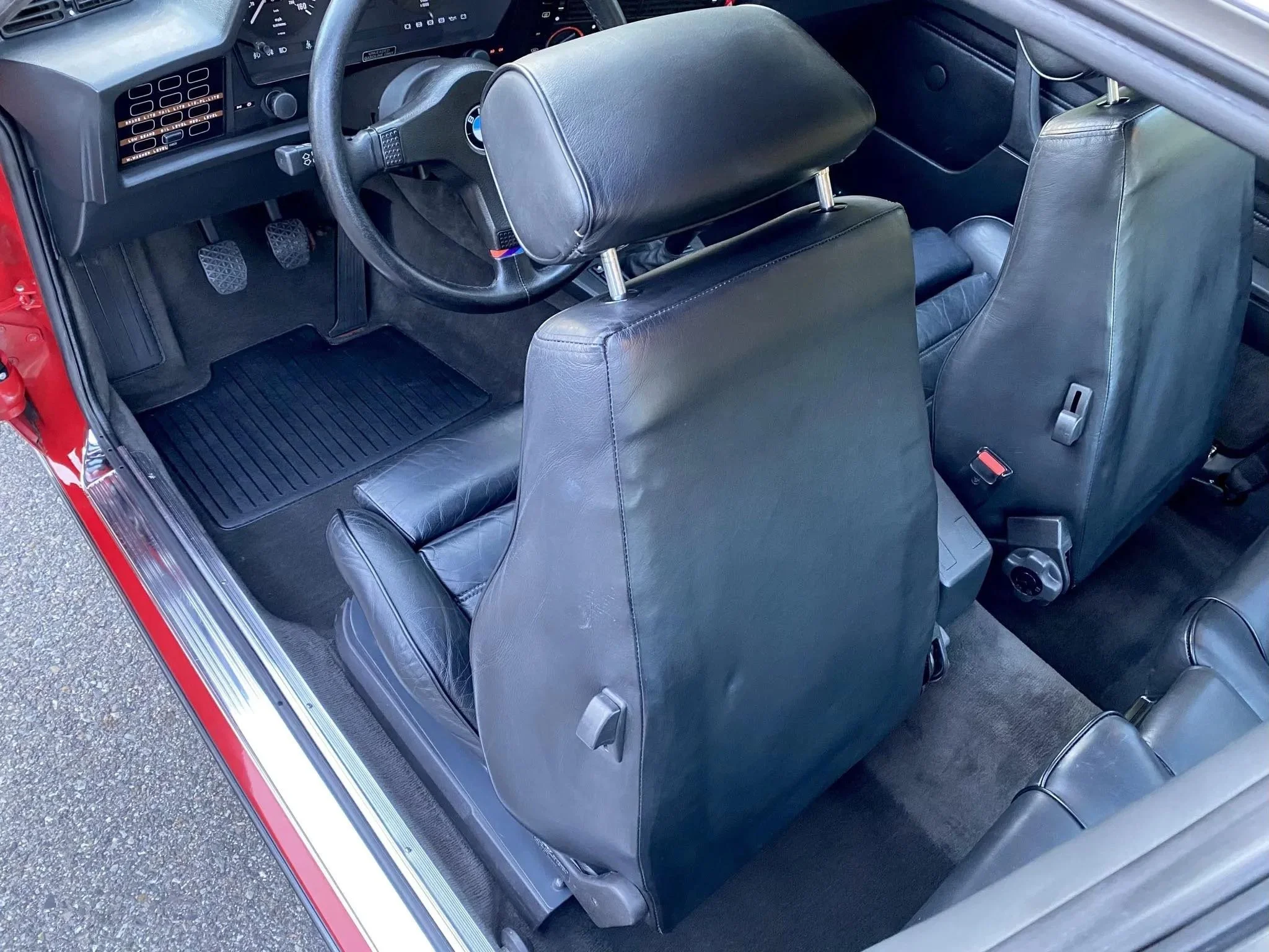 The interior of a vintage car showing black leather seats, a black steering wheel, and a dashboard with gauges and controls.