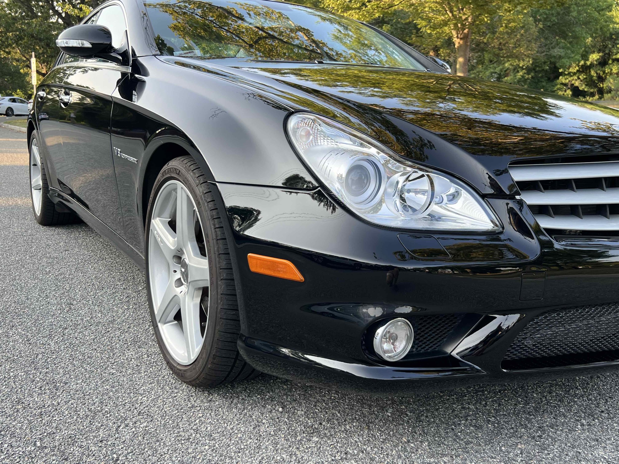 Black Mercedes-Benz convertible parked on a paved surface with trees and other vehicles in the background.