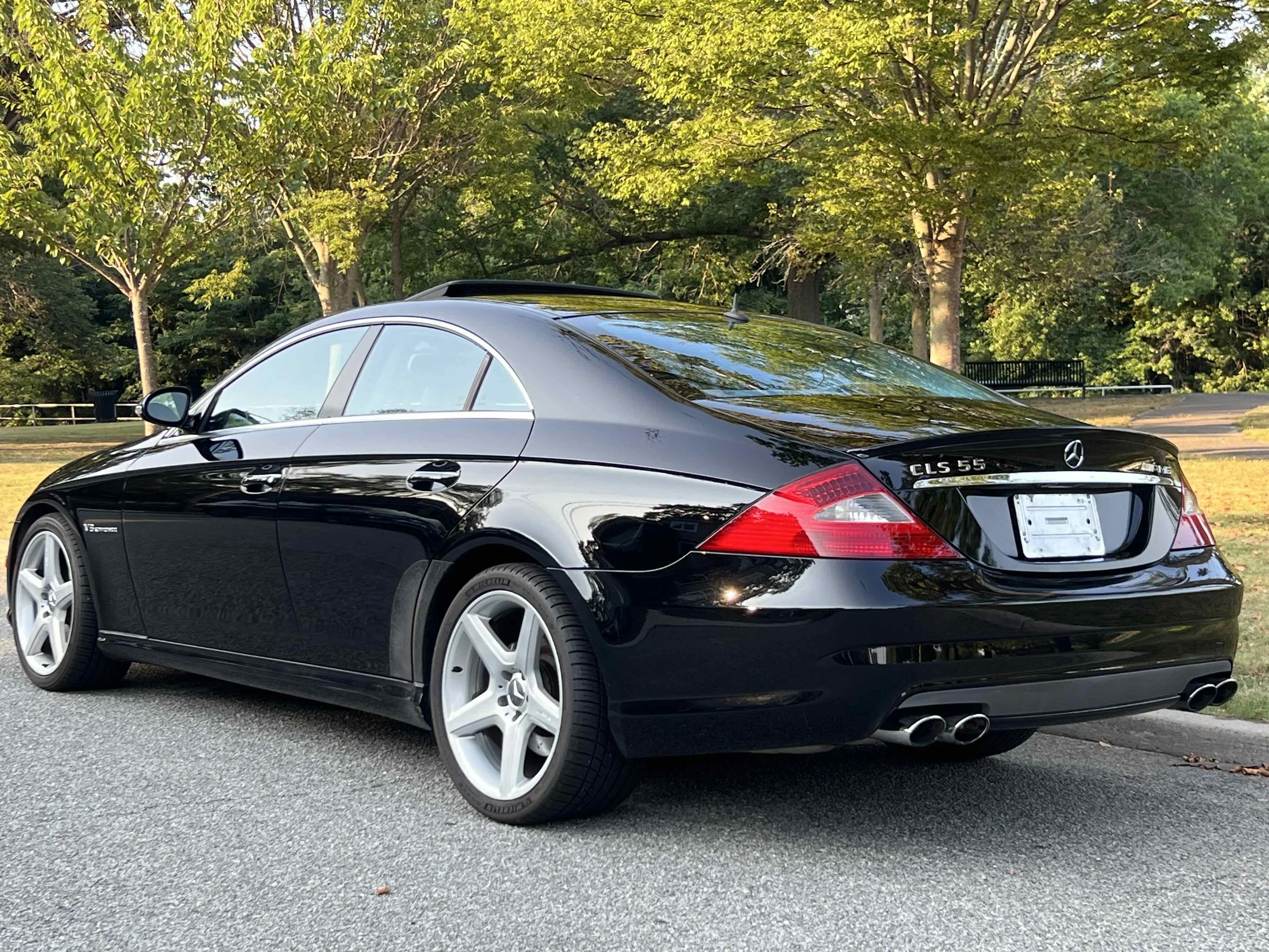 Black Mercedes-Benz CLS 55 AMG parked on a street with trees in the background.