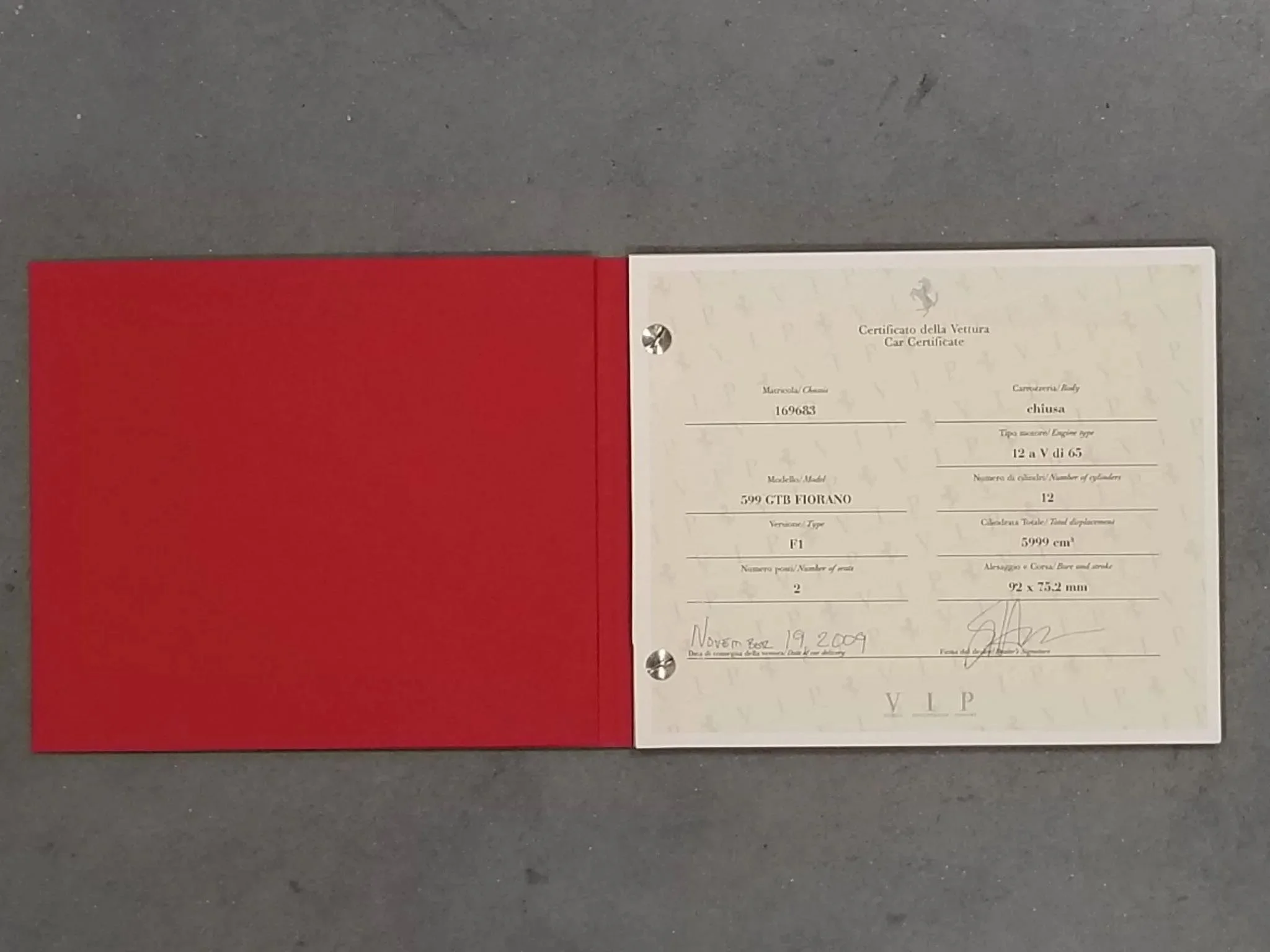 A car registration certificate on a gray surface, with a red cover folder open on the left and the certificate on the right side.