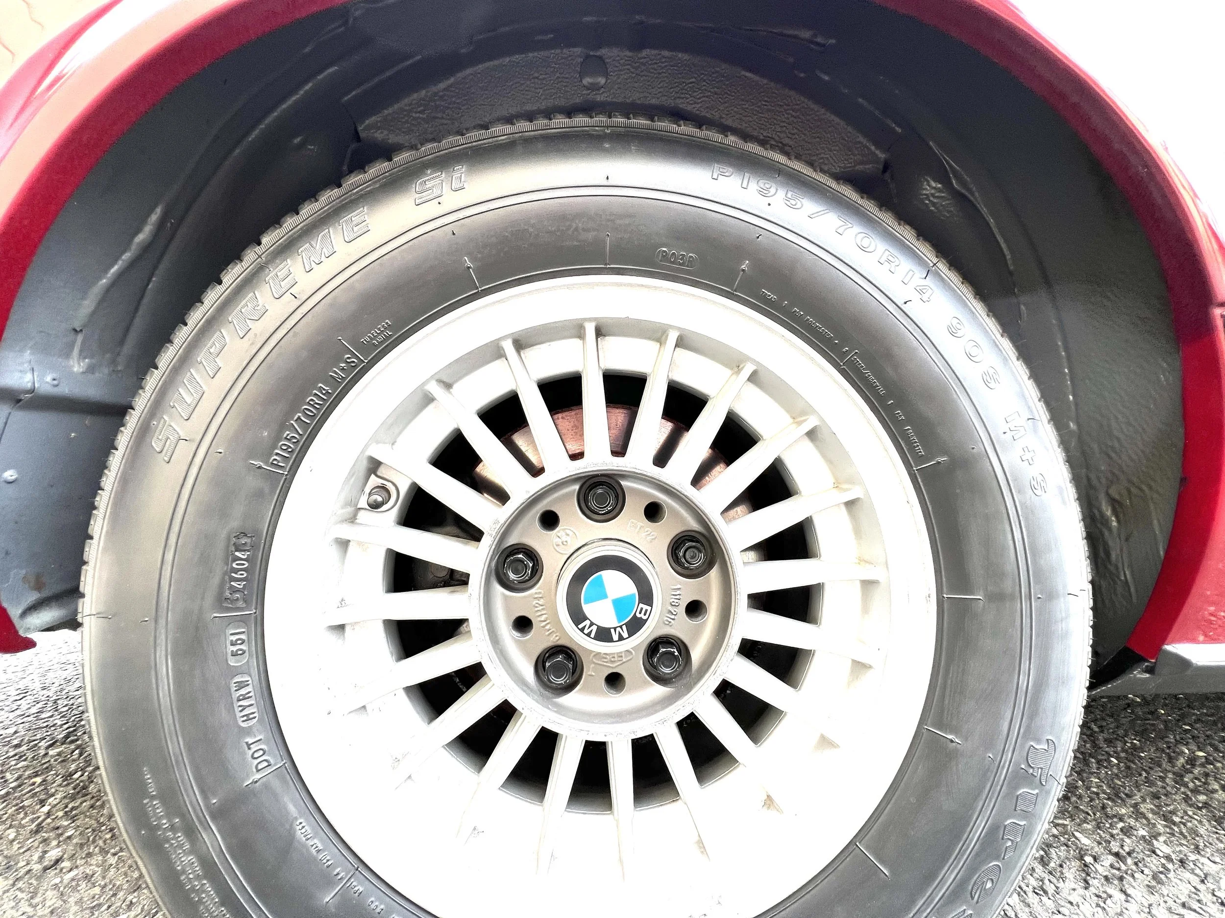 Close-up of a BMW 630 csi tire with a white BMW wheel with a BMW logo at the center, mounted on a red vehicle.
