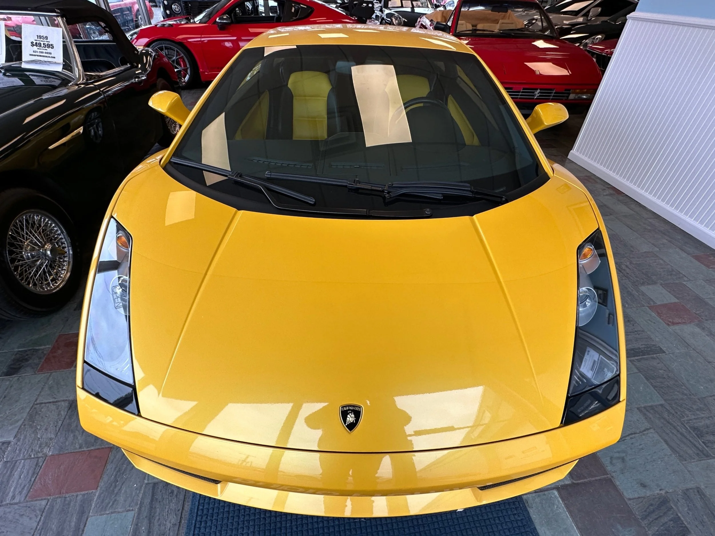 A yellow Lamborghini sports car on display in a showroom, surrounded by other classic and luxury cars.
