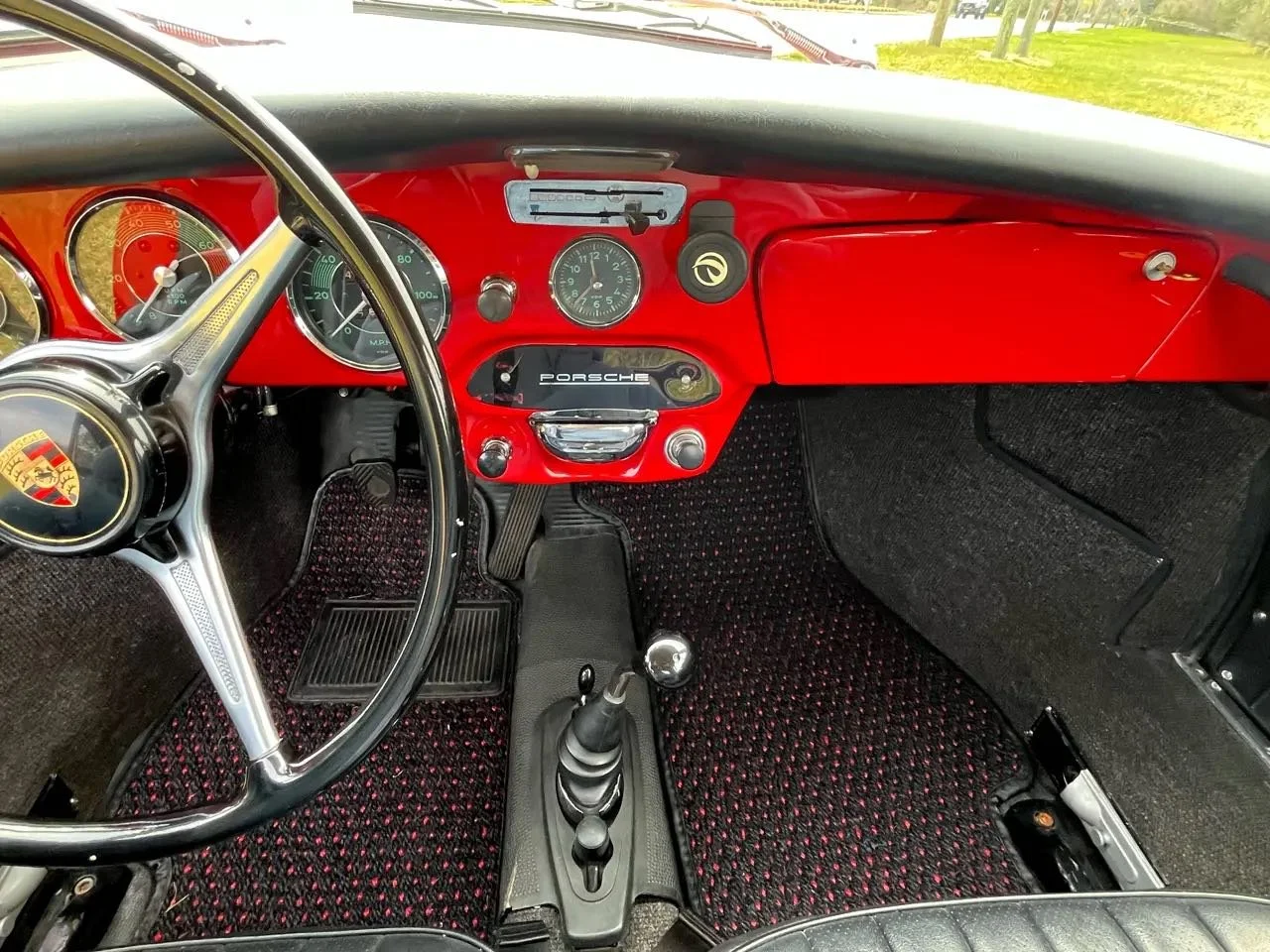 The interior of a vintage Porsche sports car with a red dashboard, black steering wheel with Porsche emblem, and a gear shift in the center console.