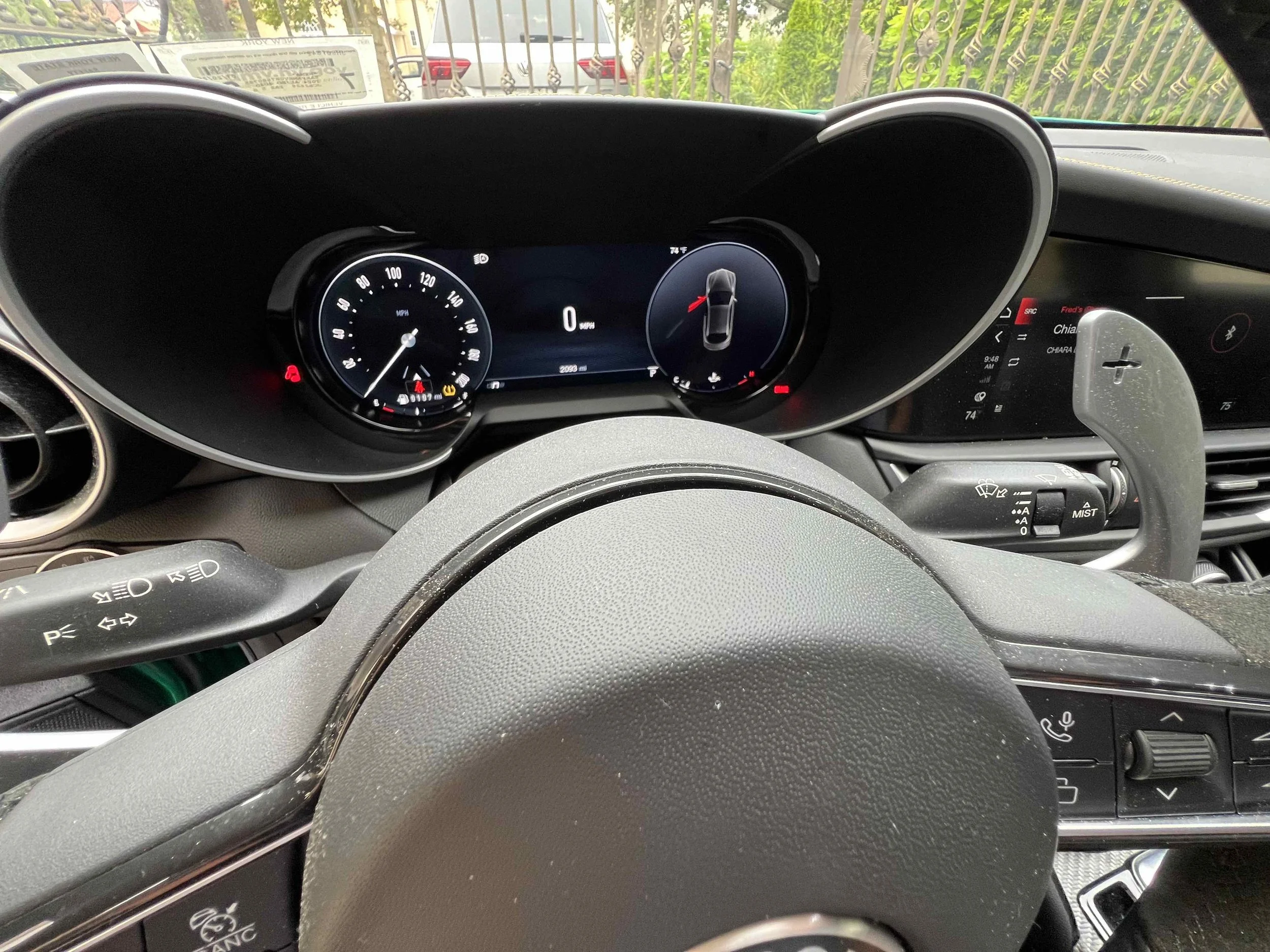 View of a car dashboard with speedometer, tachometer, and digital display, visible through the steering wheel.