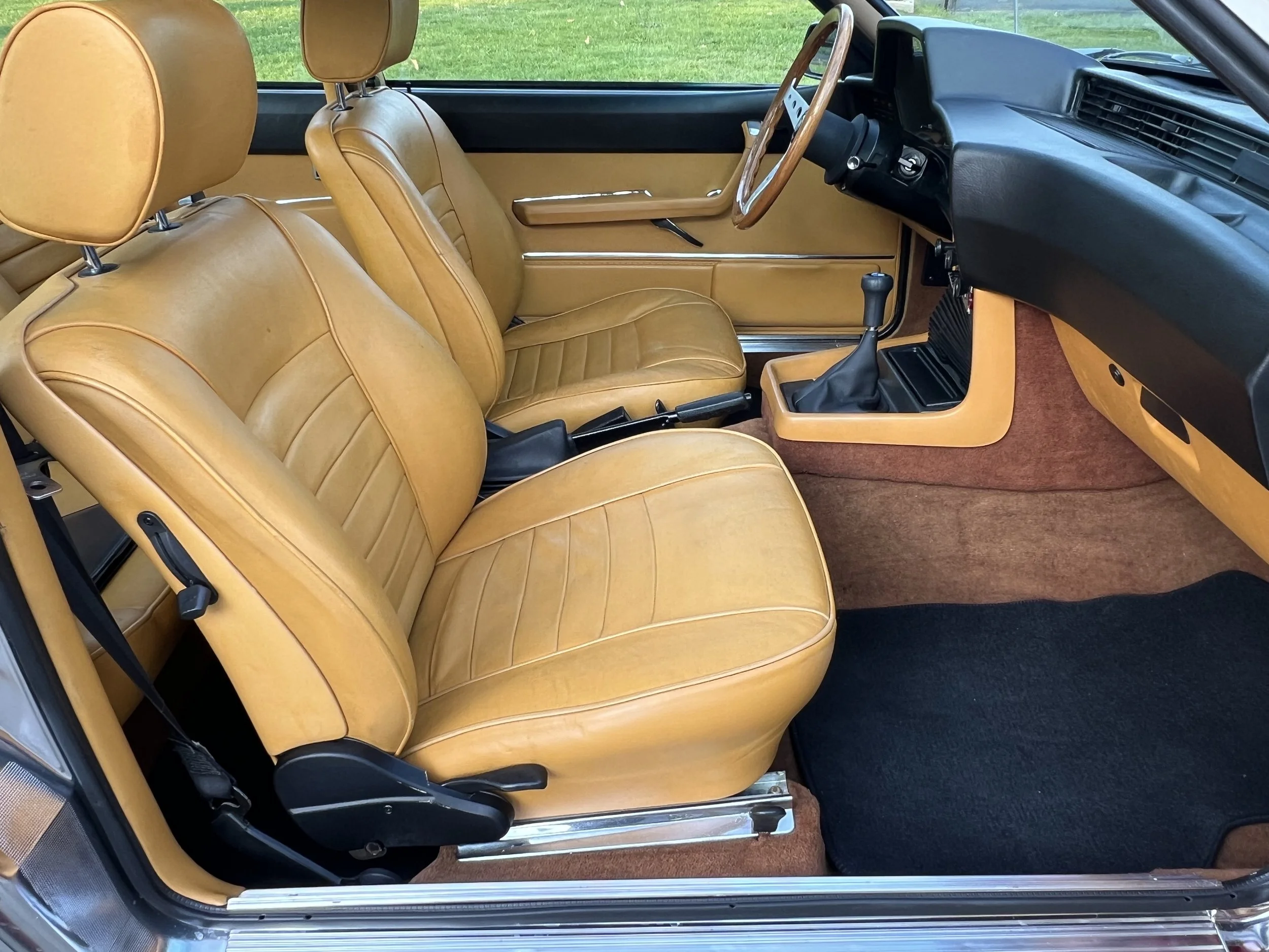 Interior of a vintage BMW 630 csi car with tan leather seats, black dashboard, gear shift, and tan carpeting.