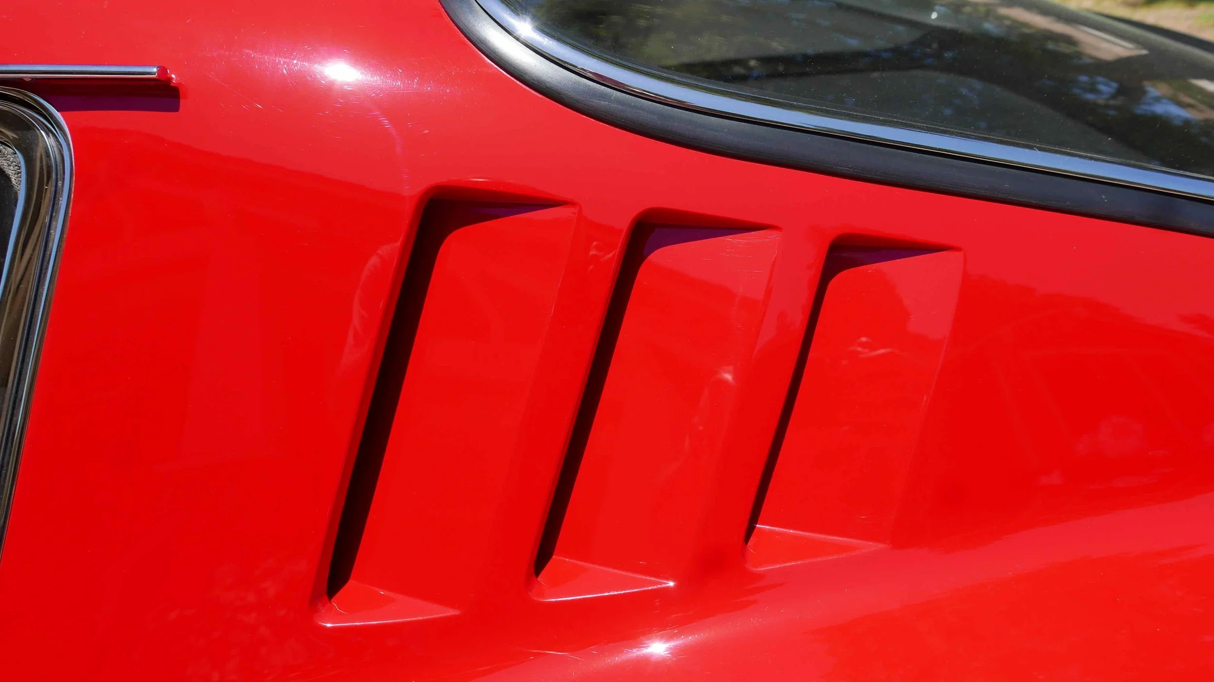 Close-up of a red car's front grille with four vertical vents