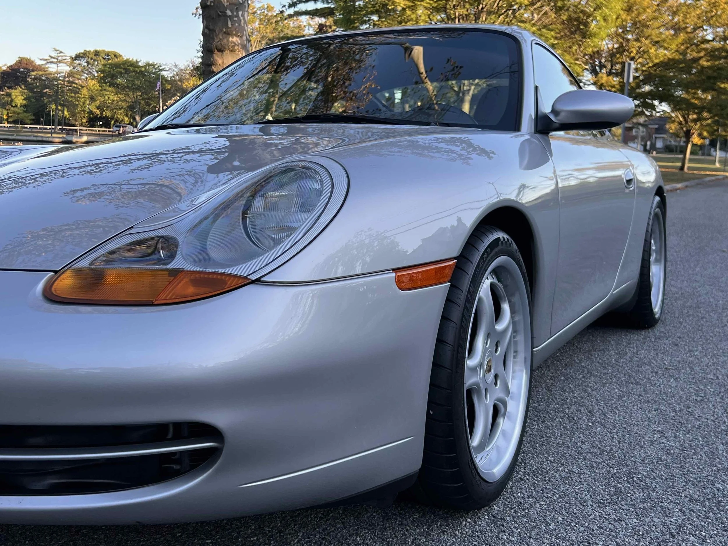 Silver Porsche convertible parked on a street with trees and houses in the background.