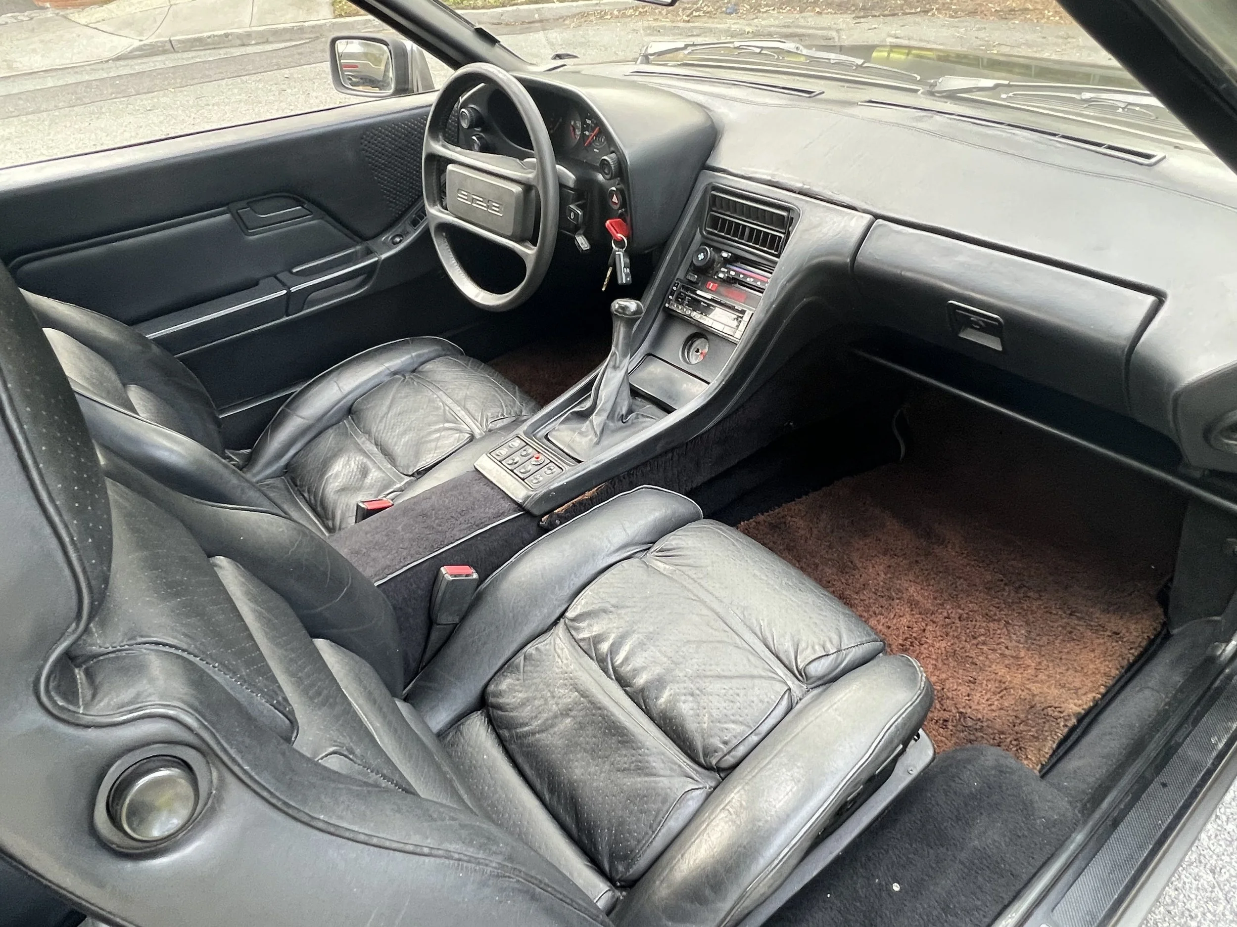 Interior of a vintage sports car with black leather seats, a manual gear shift, dashboard with analog gauges, and a steering wheel with a classic design.