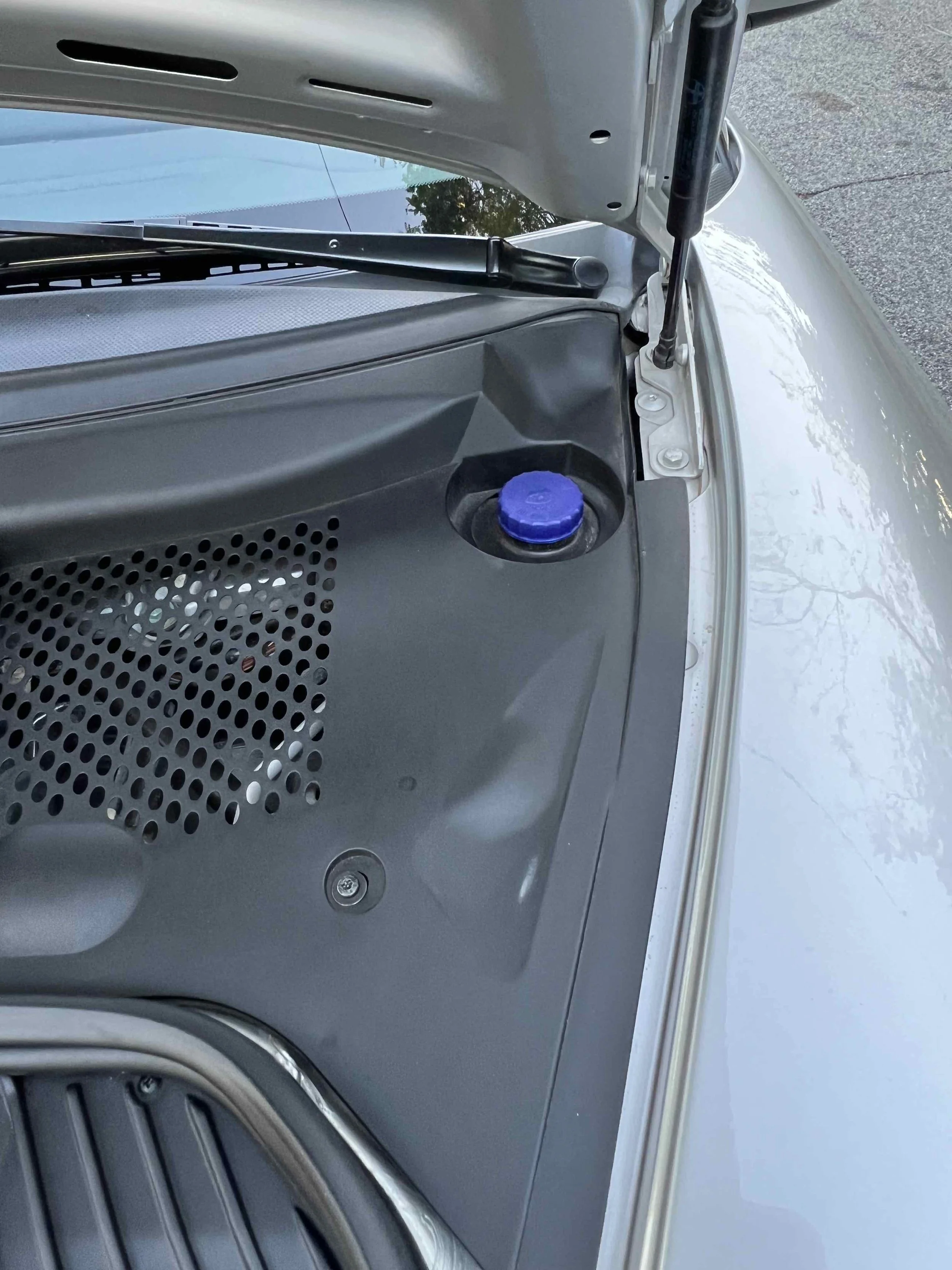Close-up of a car engine compartment with a blue cap on the right side, part of the windshield, and a partially visible windshield wiper.