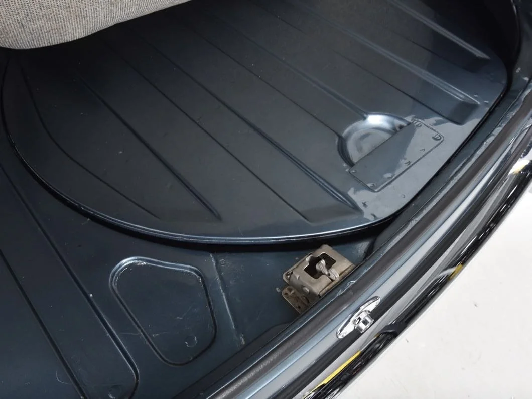 The interior of a car's trunk, showing a black rubber mat with a round indentation and a metal latch or lock.