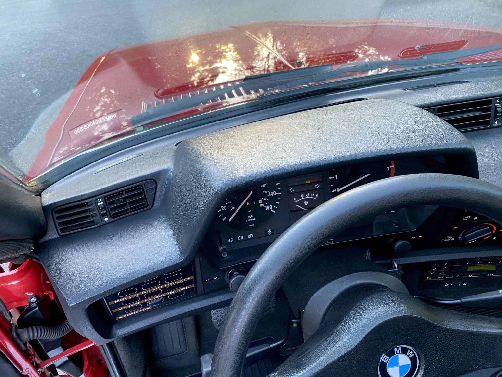 Interior of a vintage BMW car dashboard, showing speedometer, fuel gauge, and air vents with outside view through the windshield.