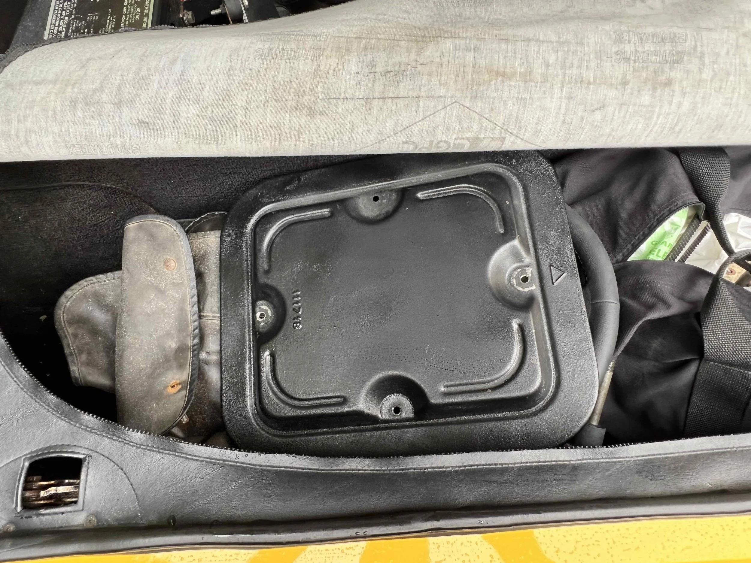 Inside a vehicle trunk, showing a black plastic compartment with a textured surface near the back seat and some fabric items around it.