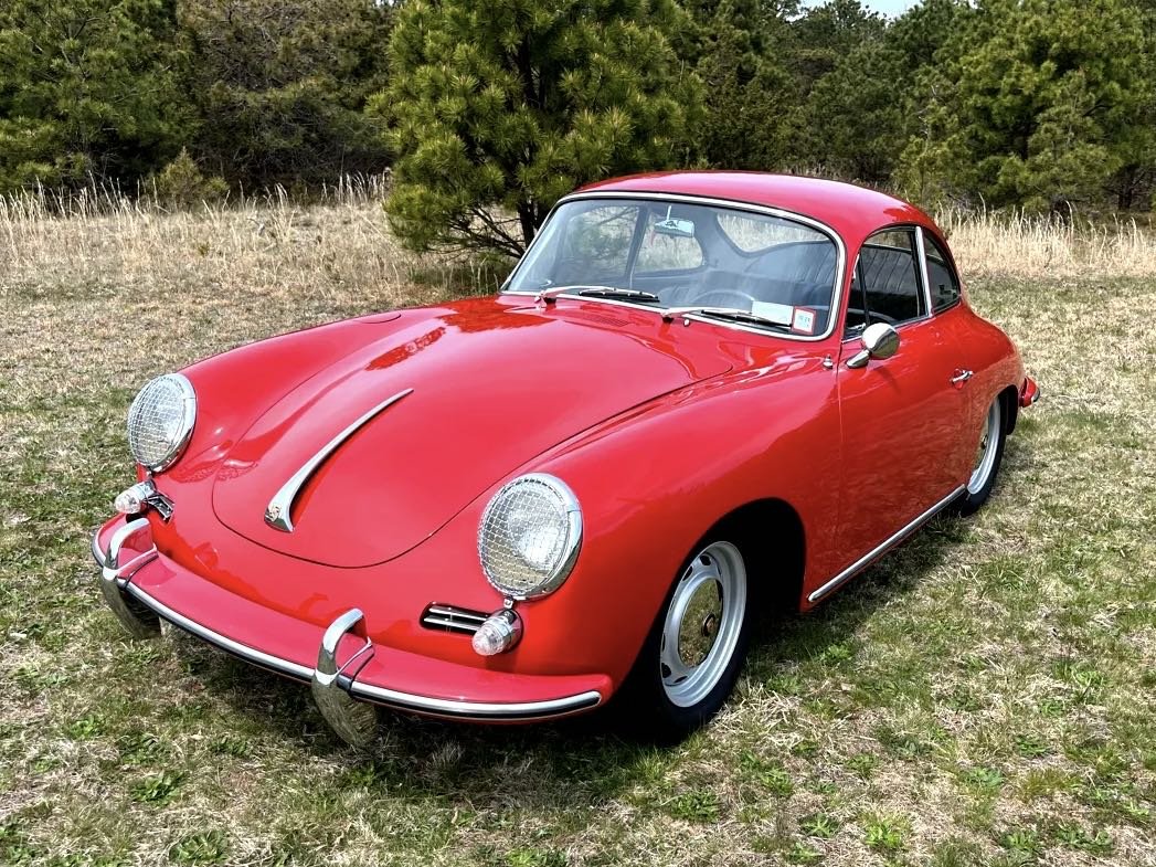 Red vintage sports car parked on grassy field with trees in the background.