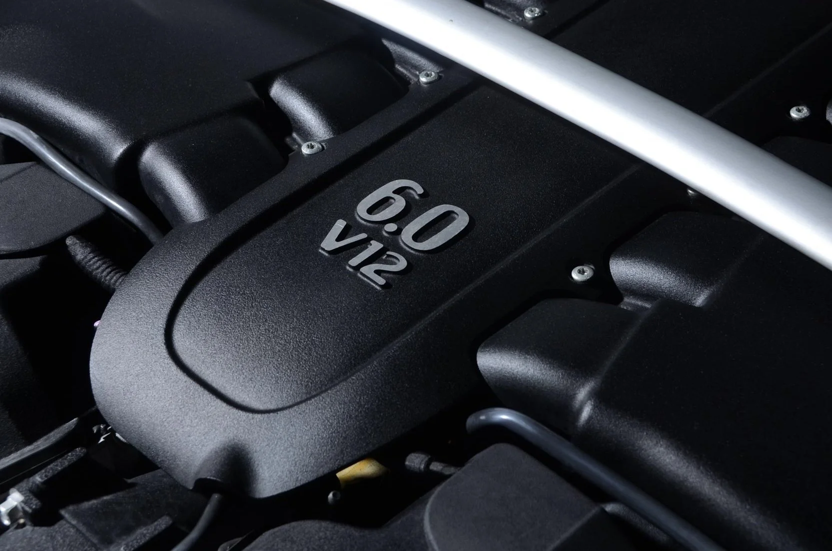 Close-up image of a car engine cover labeled '6.0 V12' in silver lettering on a black background.