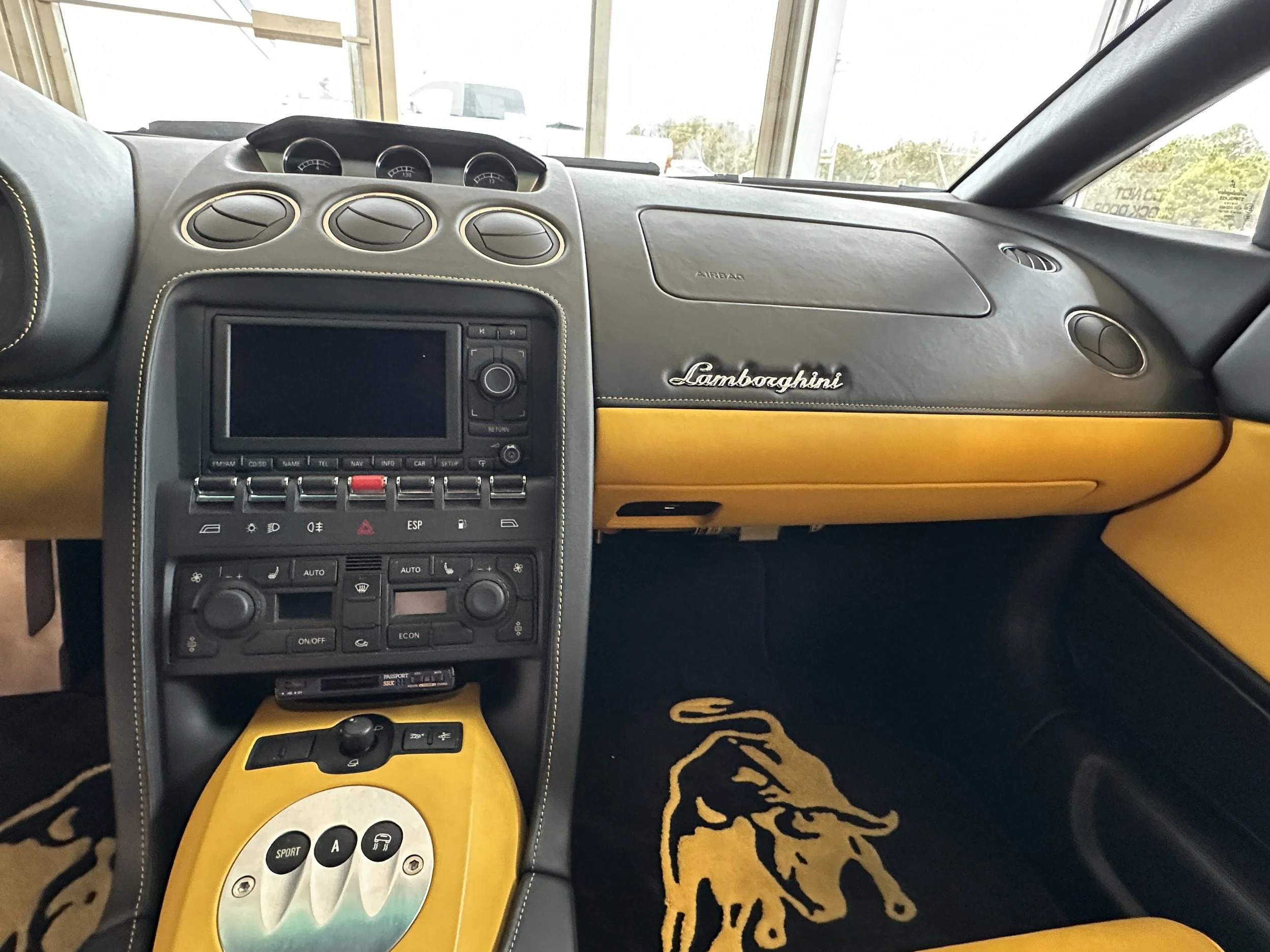 Interior of a Lamborghini sports car with black and yellow dashboard, yellow accents, and a black steering wheel.