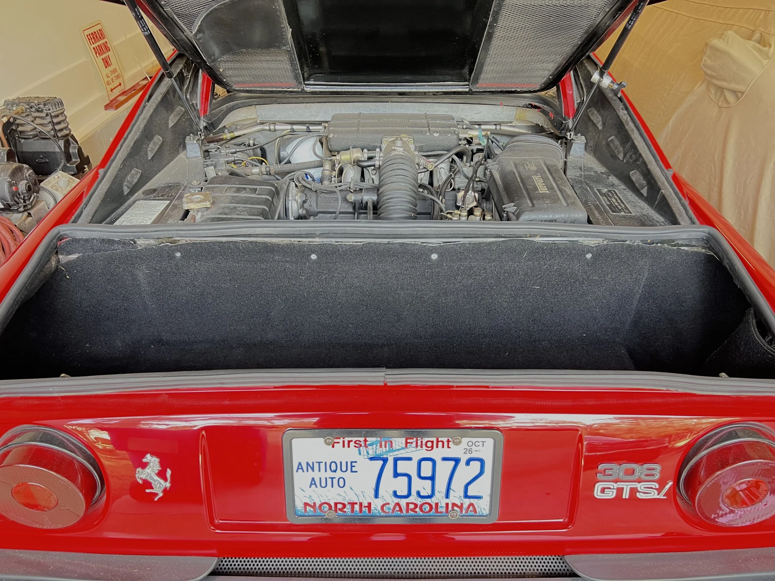Rear view of a red Ferrari 308 GTS with the engine compartment open, showing the engine and interior components.