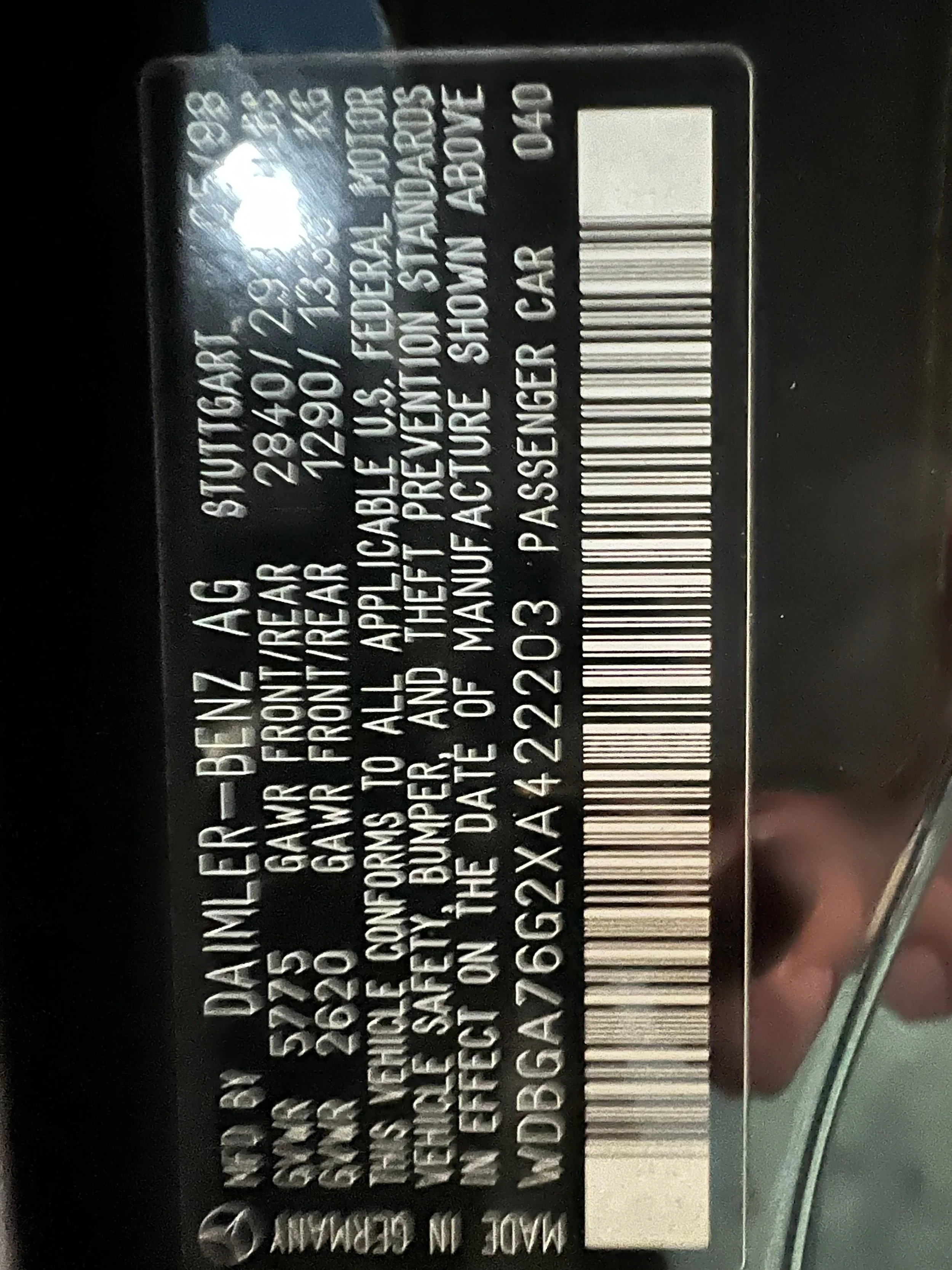 Black vehicle identification label with white text, showing manufacturing detailed information.