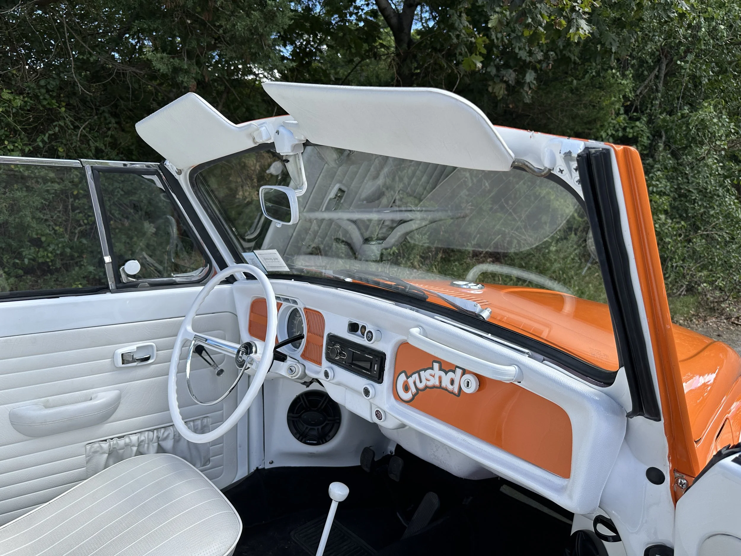 Interior of a vintage Volkswagen Type 2 camper van with white and orange color scheme and 'Crushd' sticker on the dashboard