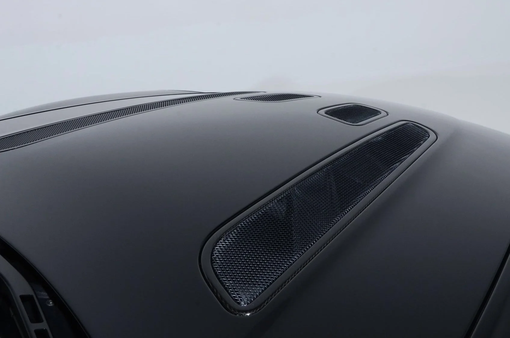 Close-up of a car hood with black vents and a matte finish.