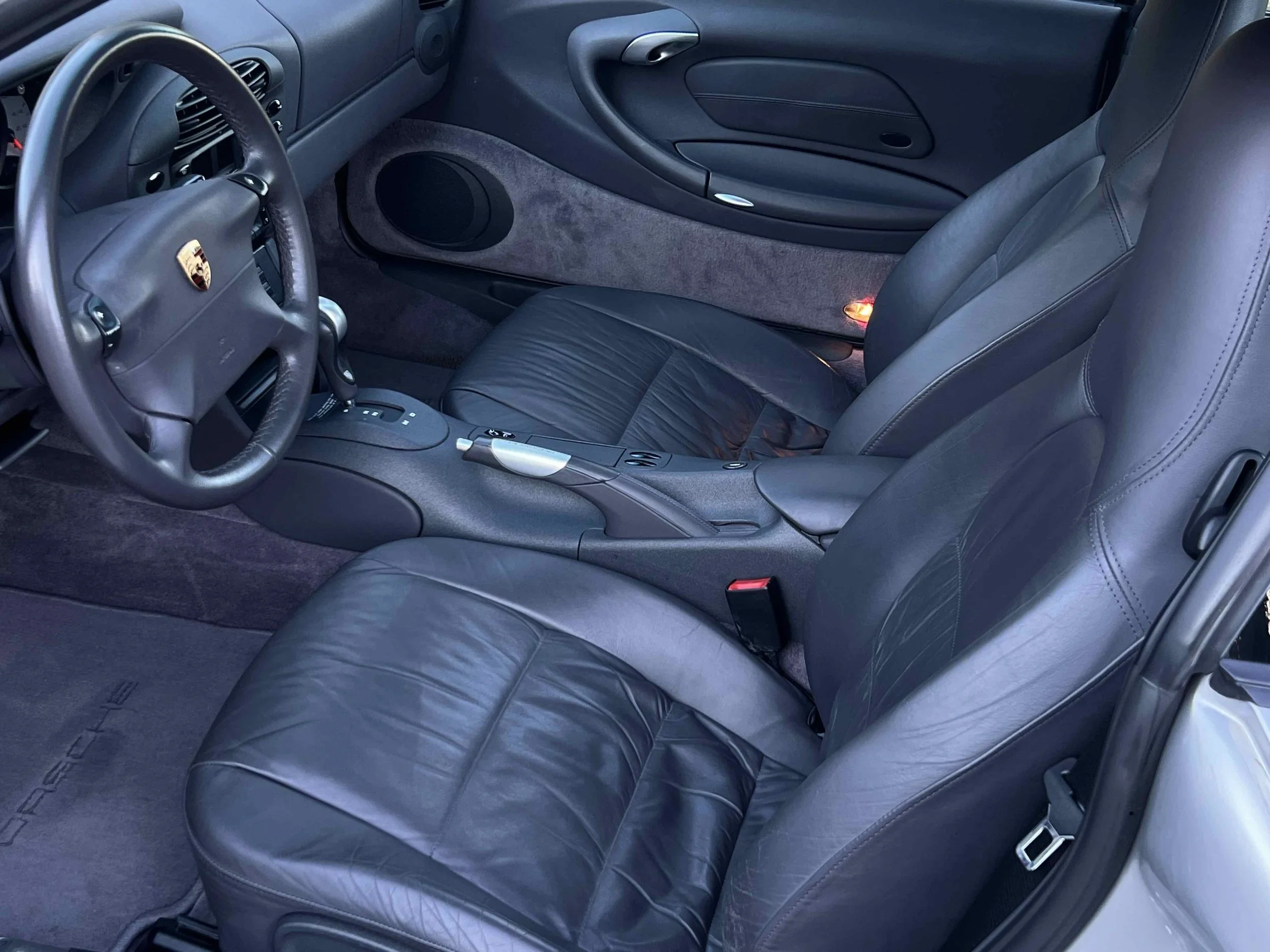 Interior of a car showing black leather seats, dashboard, steering wheel with Porsche logo, center console, and door panels.