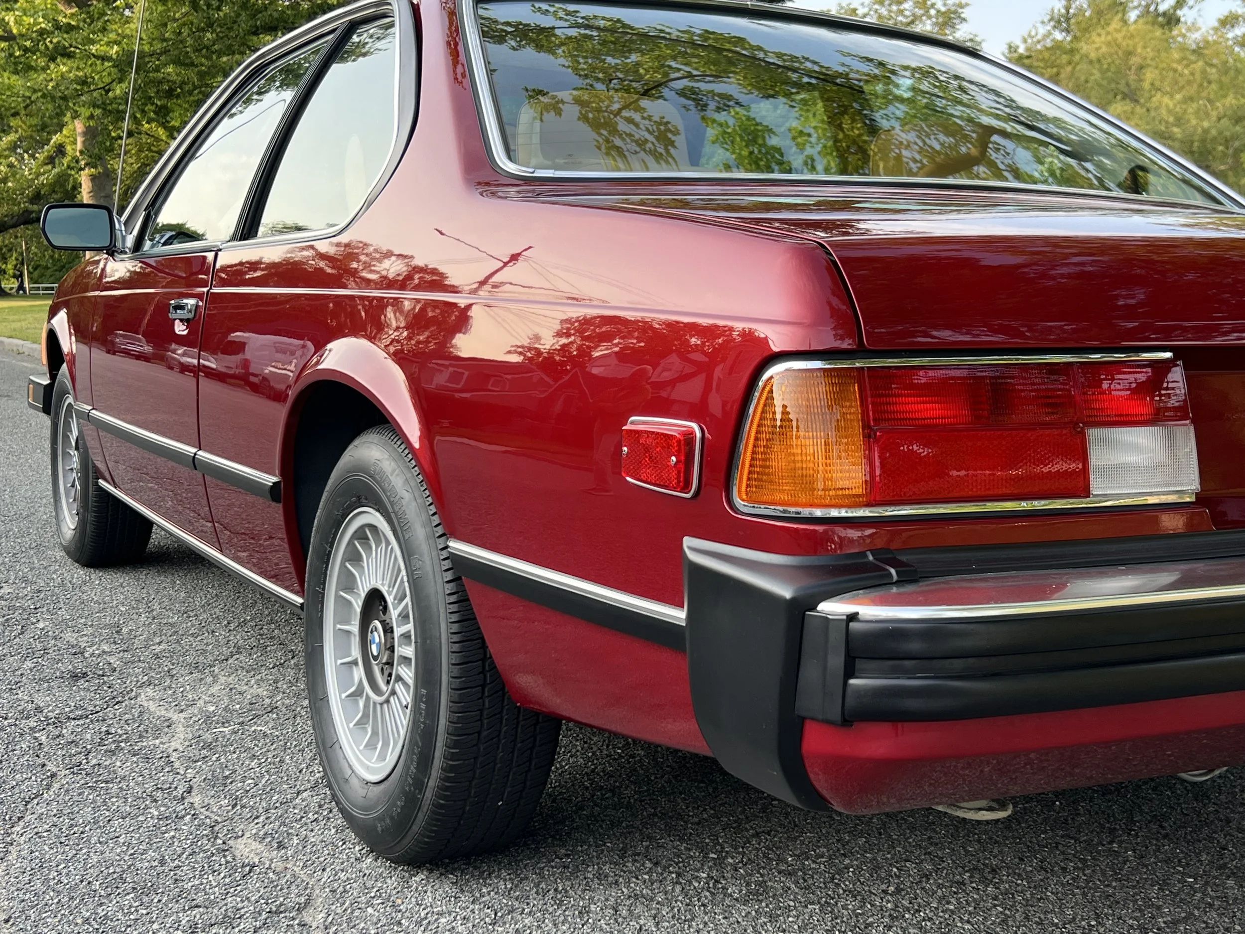 Side of Ruby Red 1977 BMW 630 csi on display in park for sale at FlowHaus