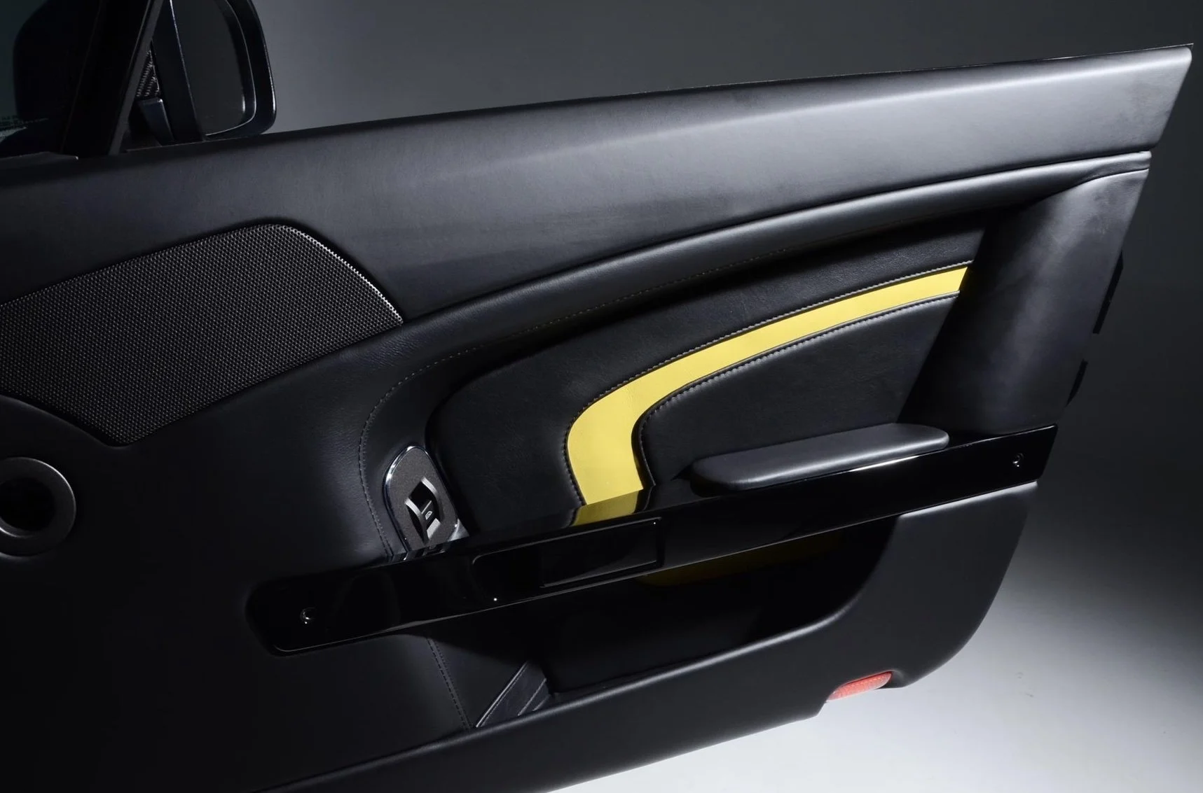 Close-up of a black car door interior with a yellow accent, a speaker grille, and a door handle.
