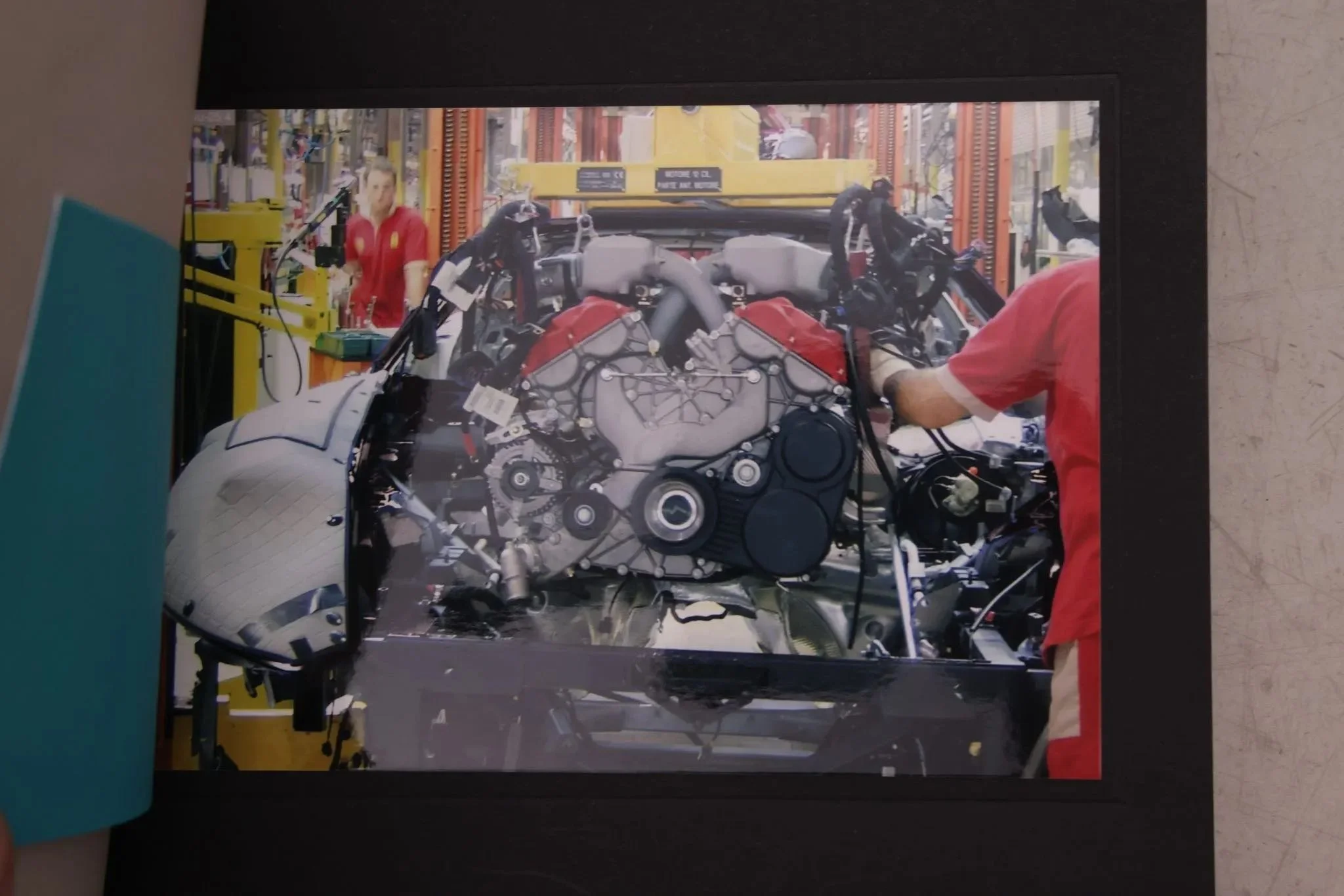 A person working on a motorcycle engine inside a workshop with another person in the background.