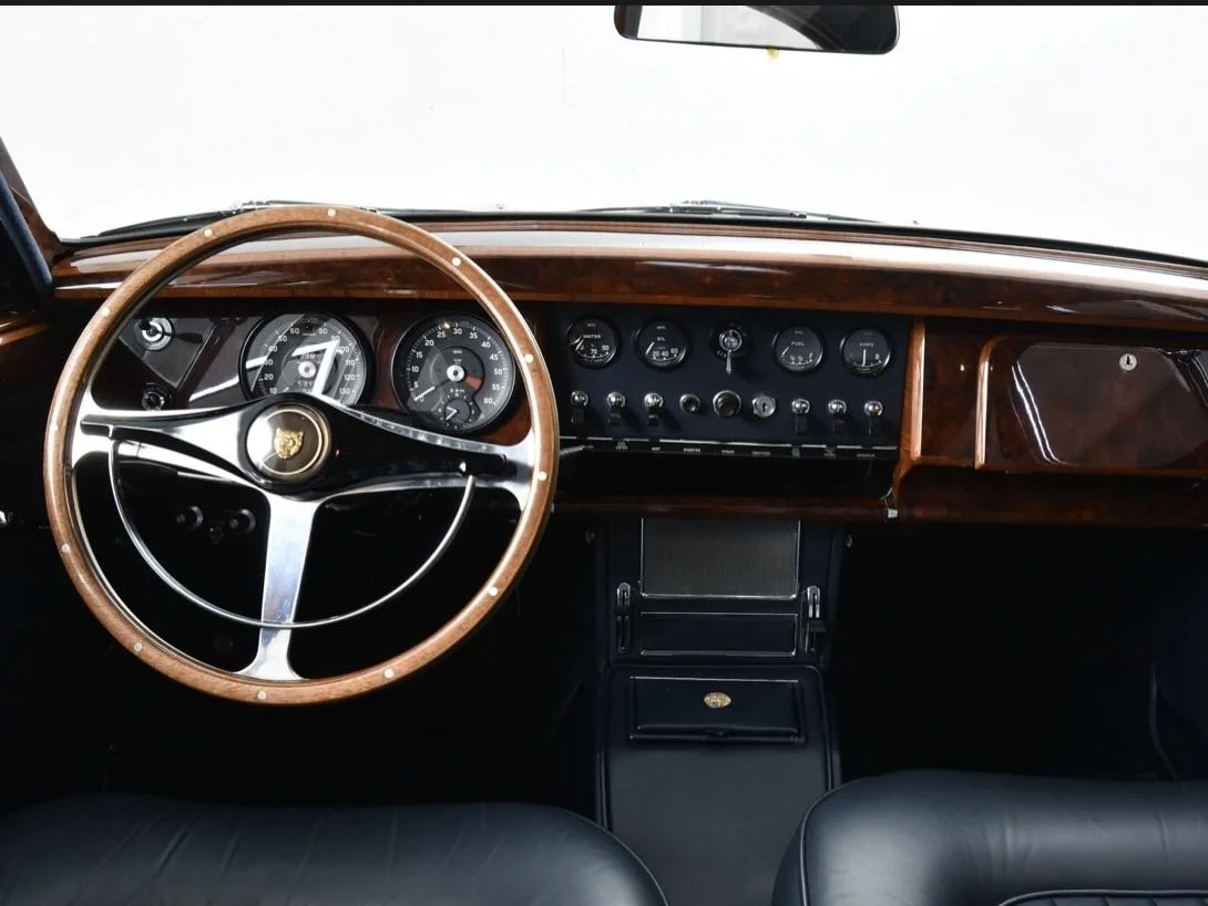 Interior of a vintage car dashboard with a wooden steering wheel, analog gauges, and control buttons.