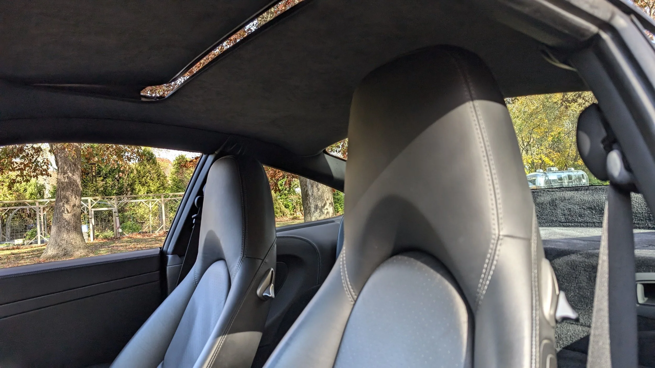 View of the interior of a car, showing two front seats with a background of trees and a fence outside the window.
