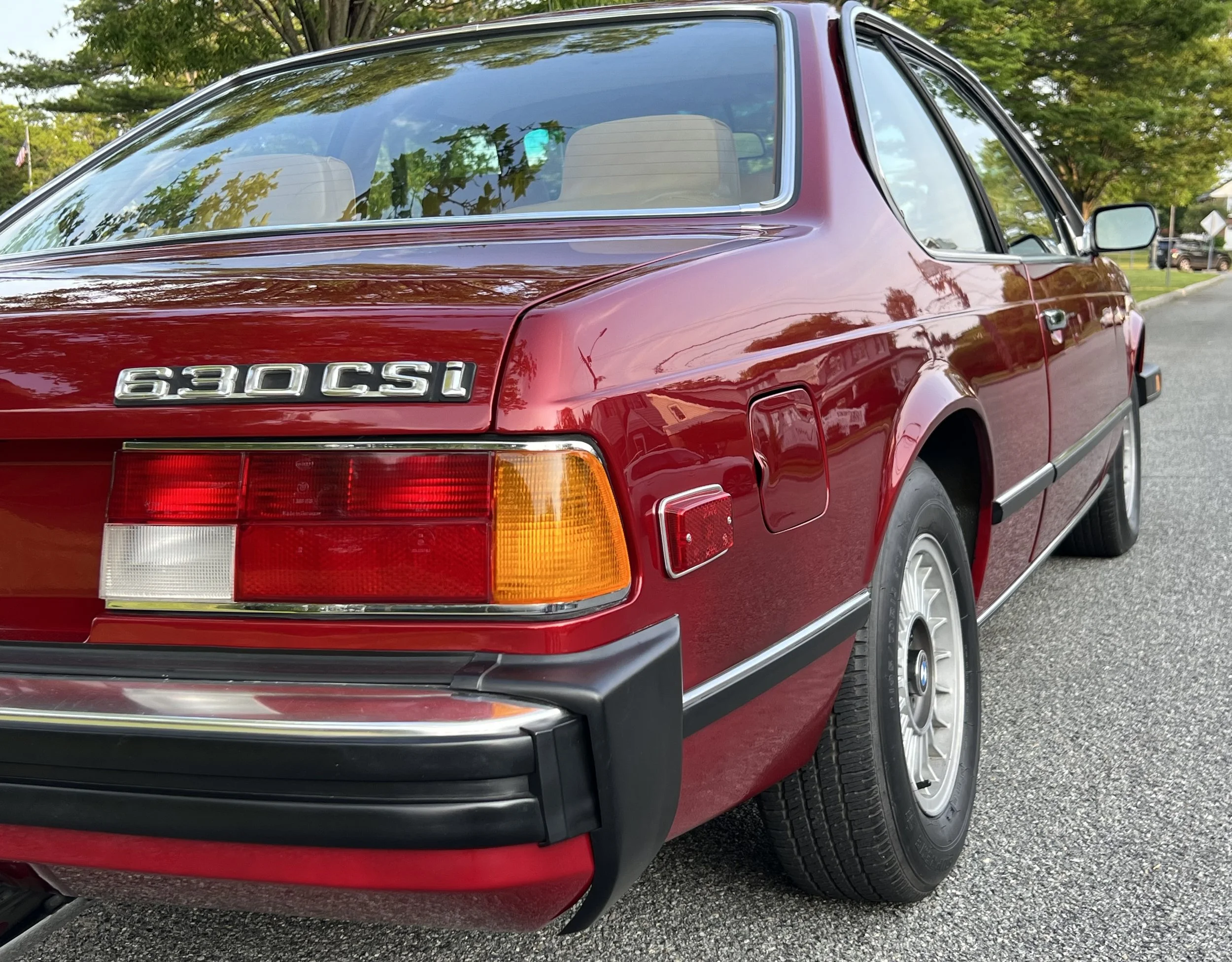 Red BMW 630 CSI classic car parked on a street with trees and a grassy area in the background.