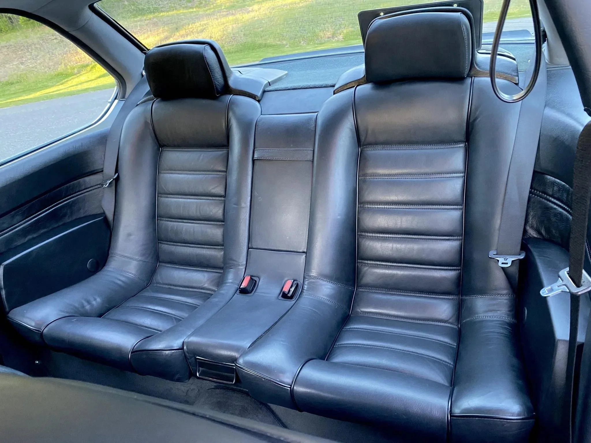 Back seat of a car with black leather upholstery, two headrests, and seat belts.